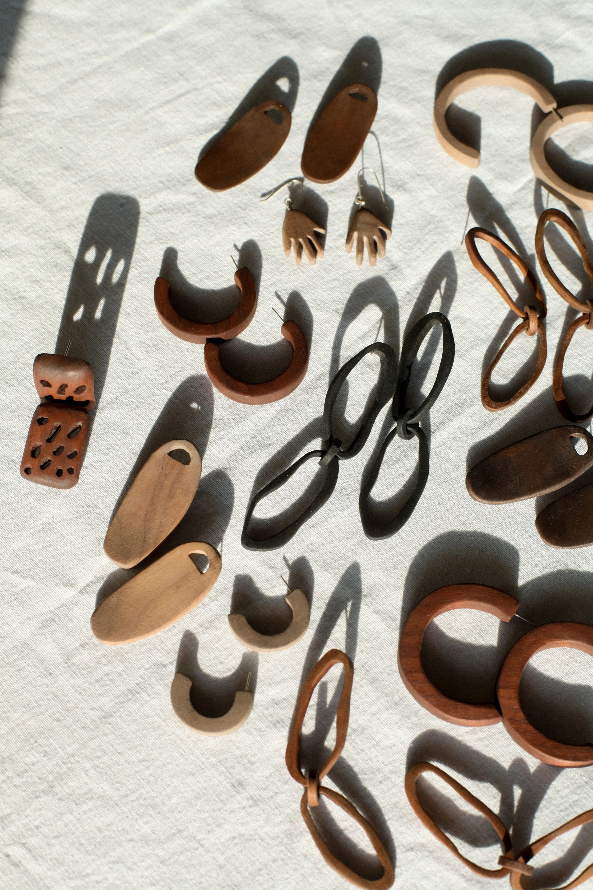 Various jewelry pieces including earrings, bracelets, and rings made of wood, displayed on a white fabric surface with sunlight casting shadows.