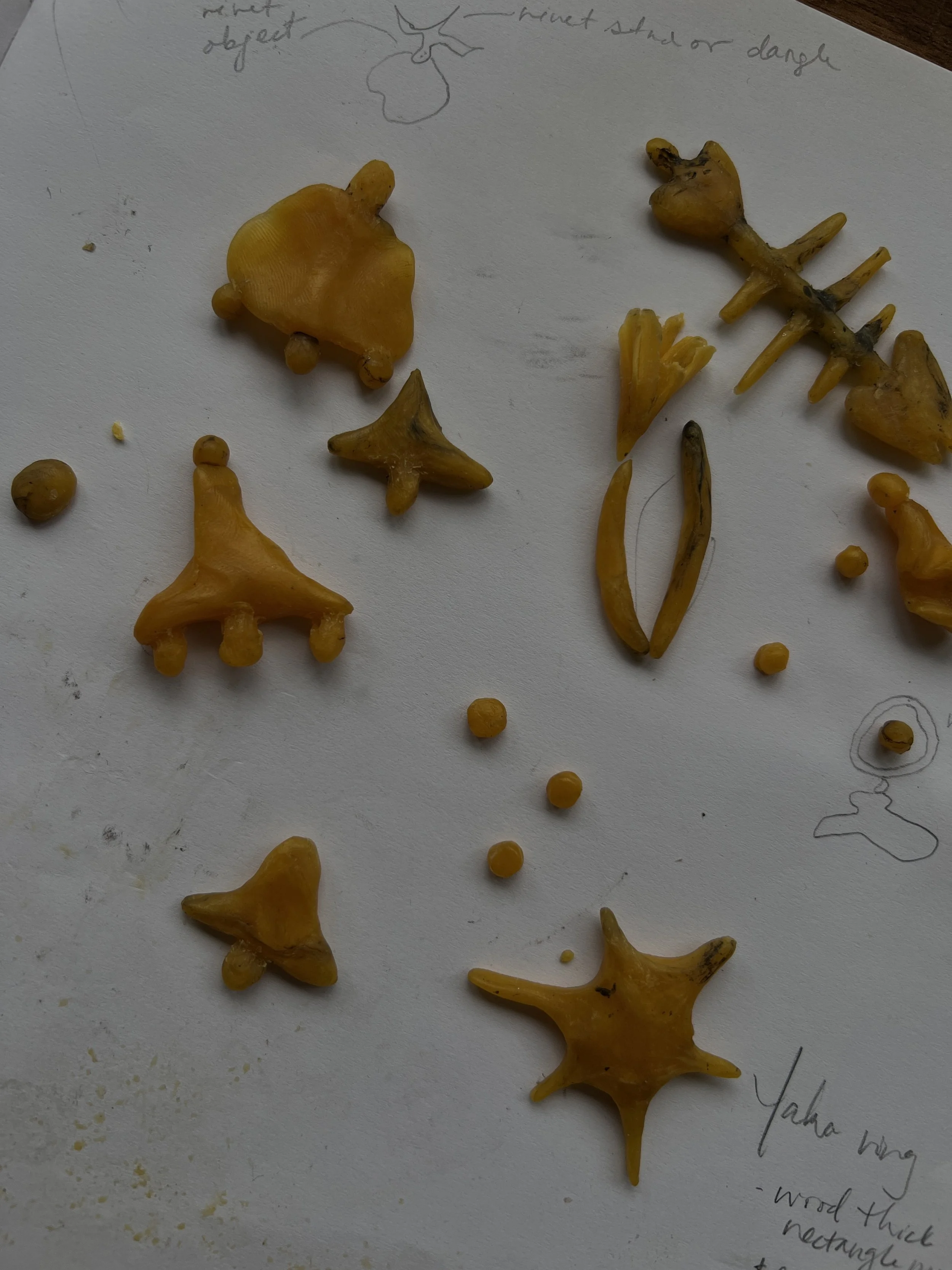 Various yellow-orange molded pieces of beeswax displayed on a paper with sketches and notes at the top and bottom.