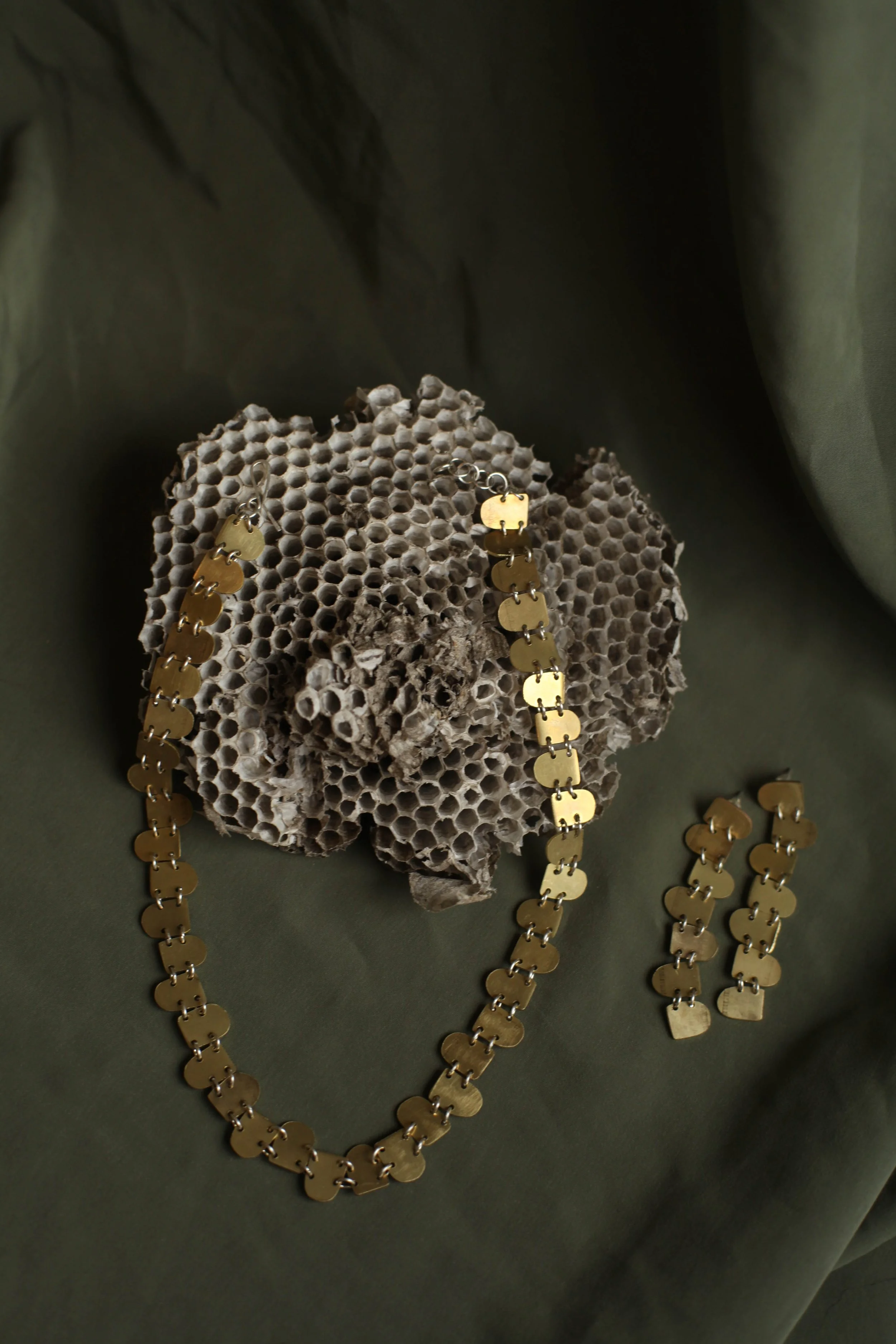 Brass jewelry necklace and earrings displayed on a piece of honeycomb and fabric background.