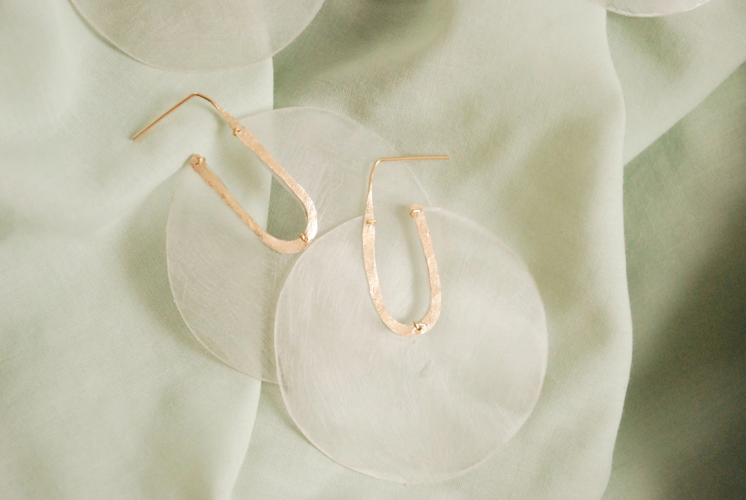 Gold textured hoop earrings with textured plastic water bottle, set on a soft green fabric background.