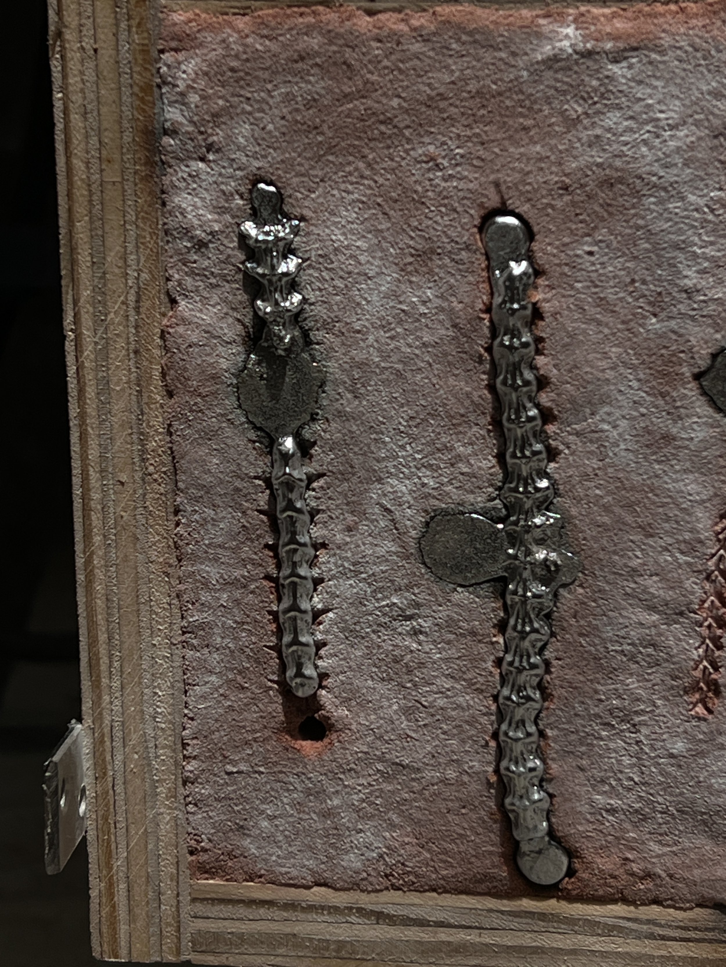 Two aluminum snake vertebrae casts in a delft clay casting box