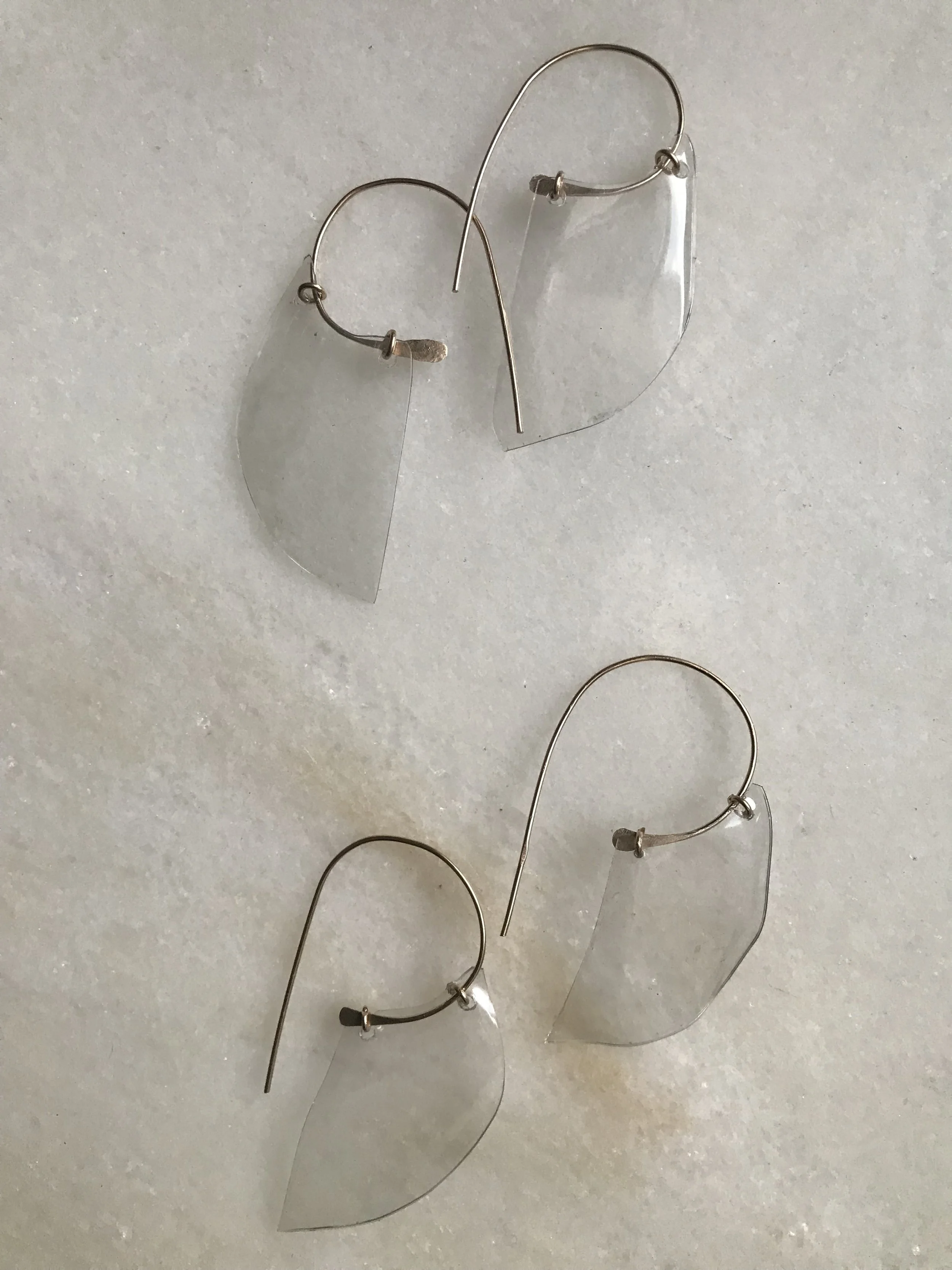 A pair of earrings with clear, semi-circle plastic water bottle bases and gold hooks, laid on a white surface.