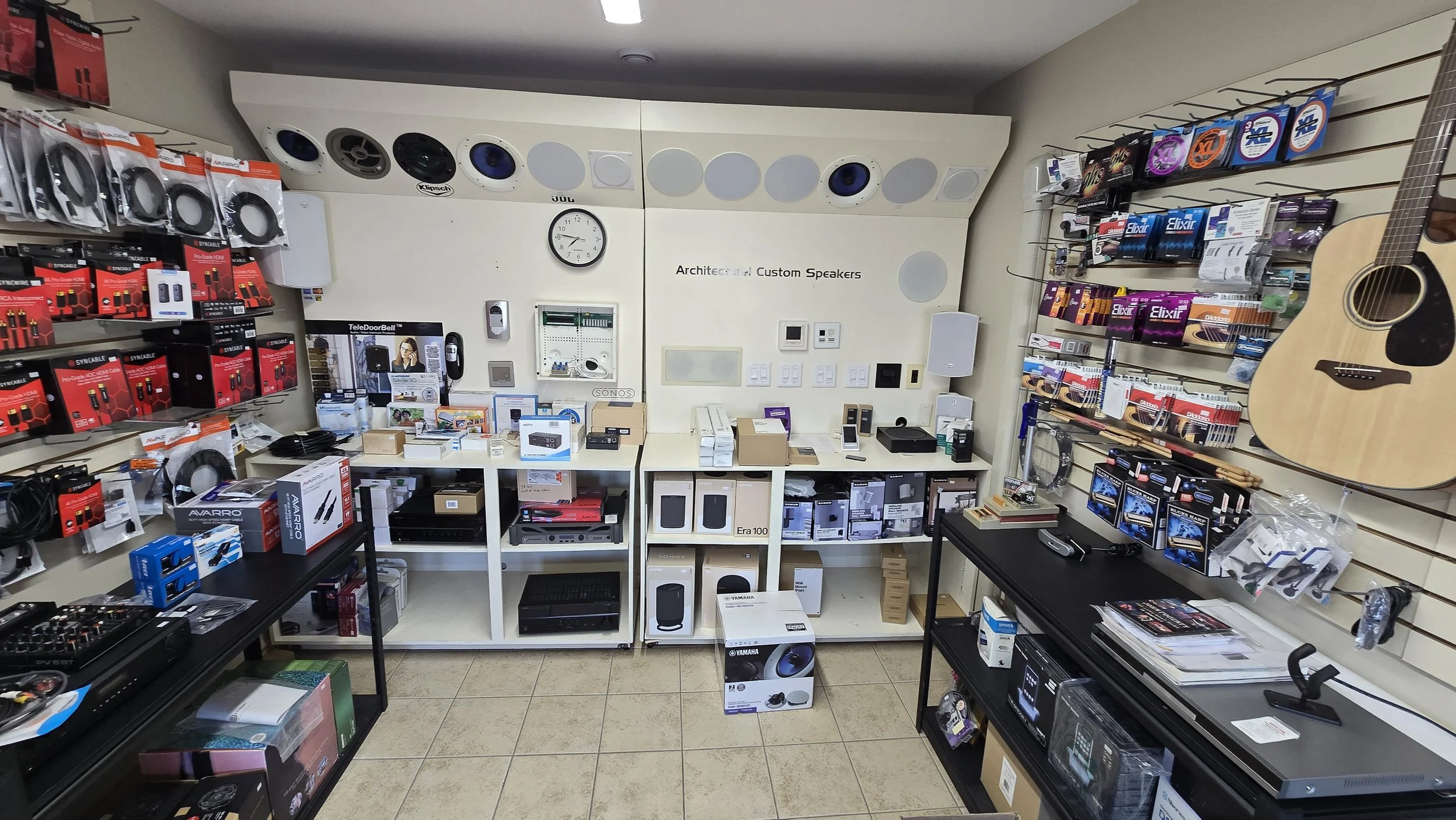 Interior of an electronics store with shelves displaying audio equipment, cables, and accessories, along with musical instruments like an acoustic guitar on the wall.