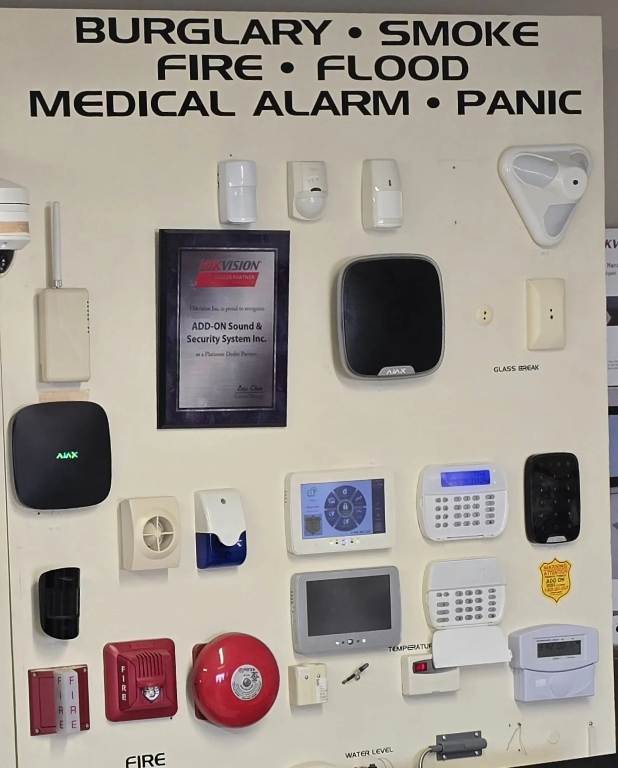 A wall display of various security, fire, smoke, flood, medical alarm, and panic alarm devices in a security system showroom.
