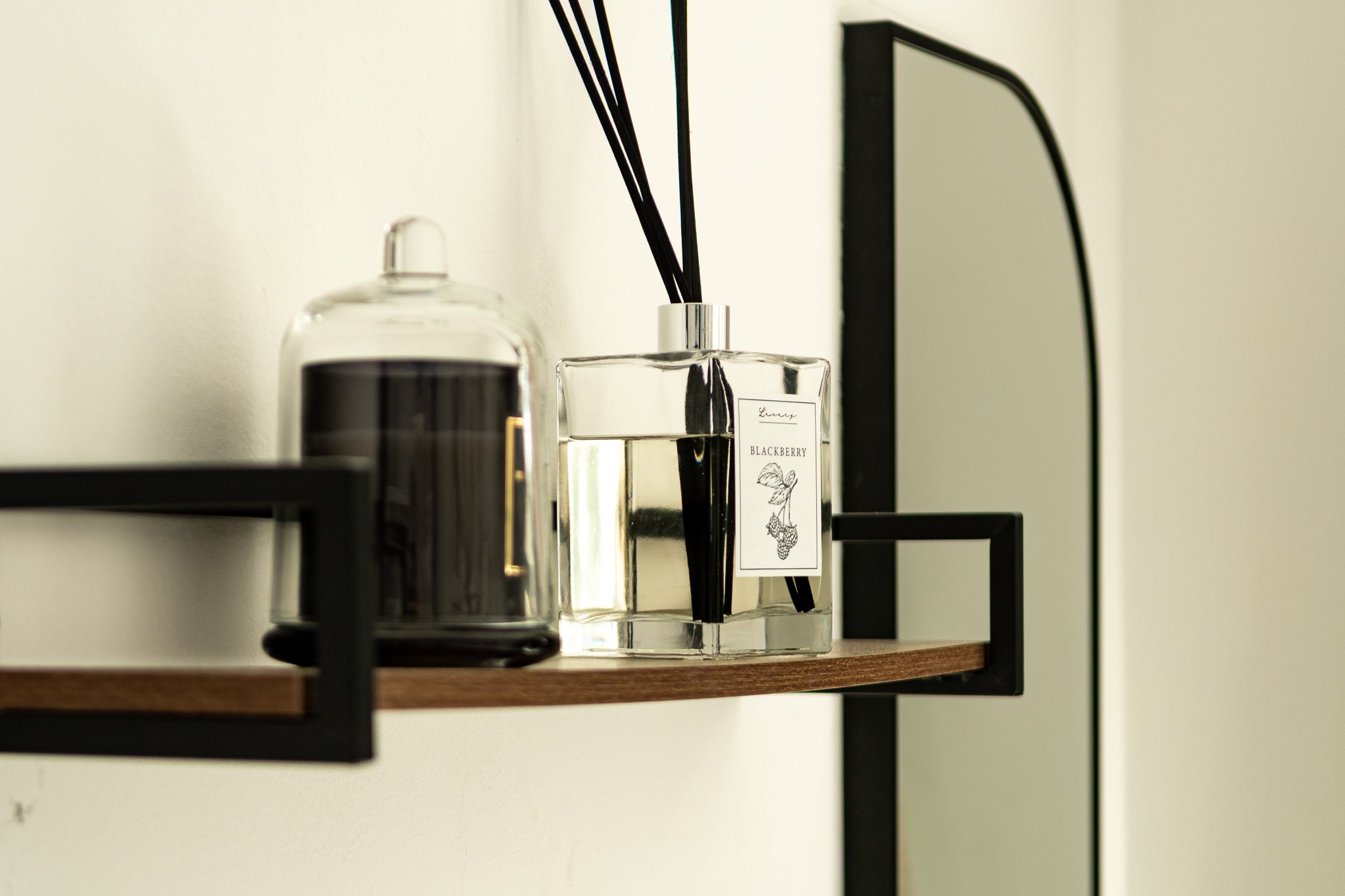 Decorative shelf with a black candle in a glass container and a reed diffuser with a blackberry scent label