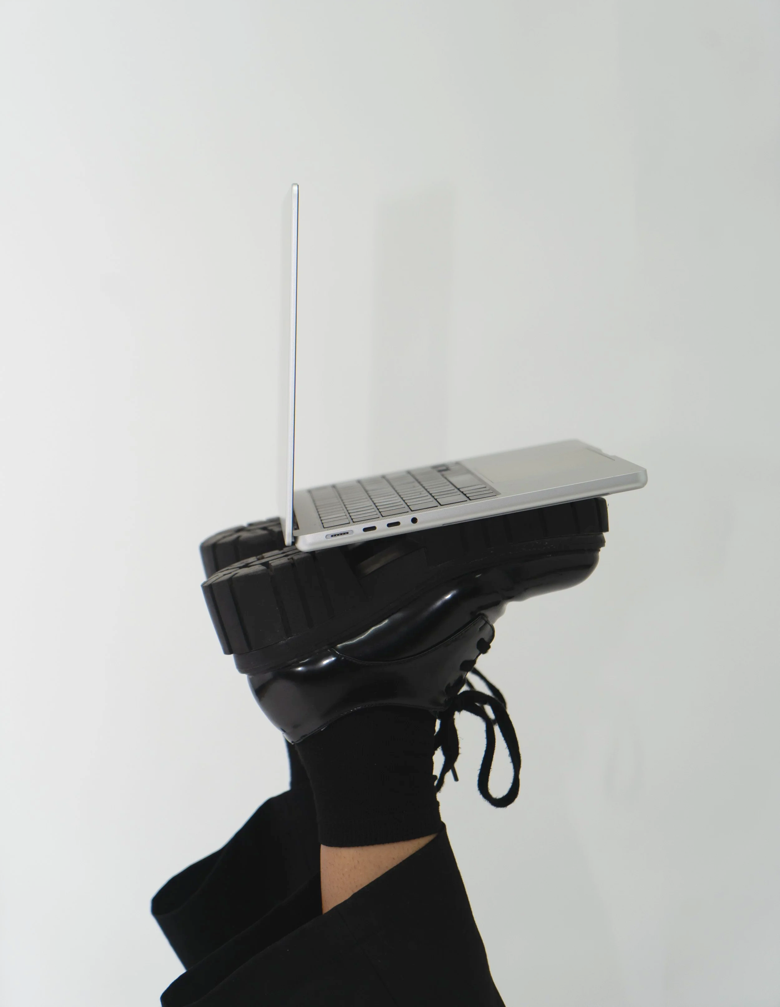 A person wearing black shoes and black pants balancing on one foot, with a laptop balanced on their shoe against a plain white background.