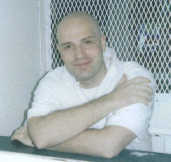 Randy Halprin in a visitation booth, smiling with his arms crossed.