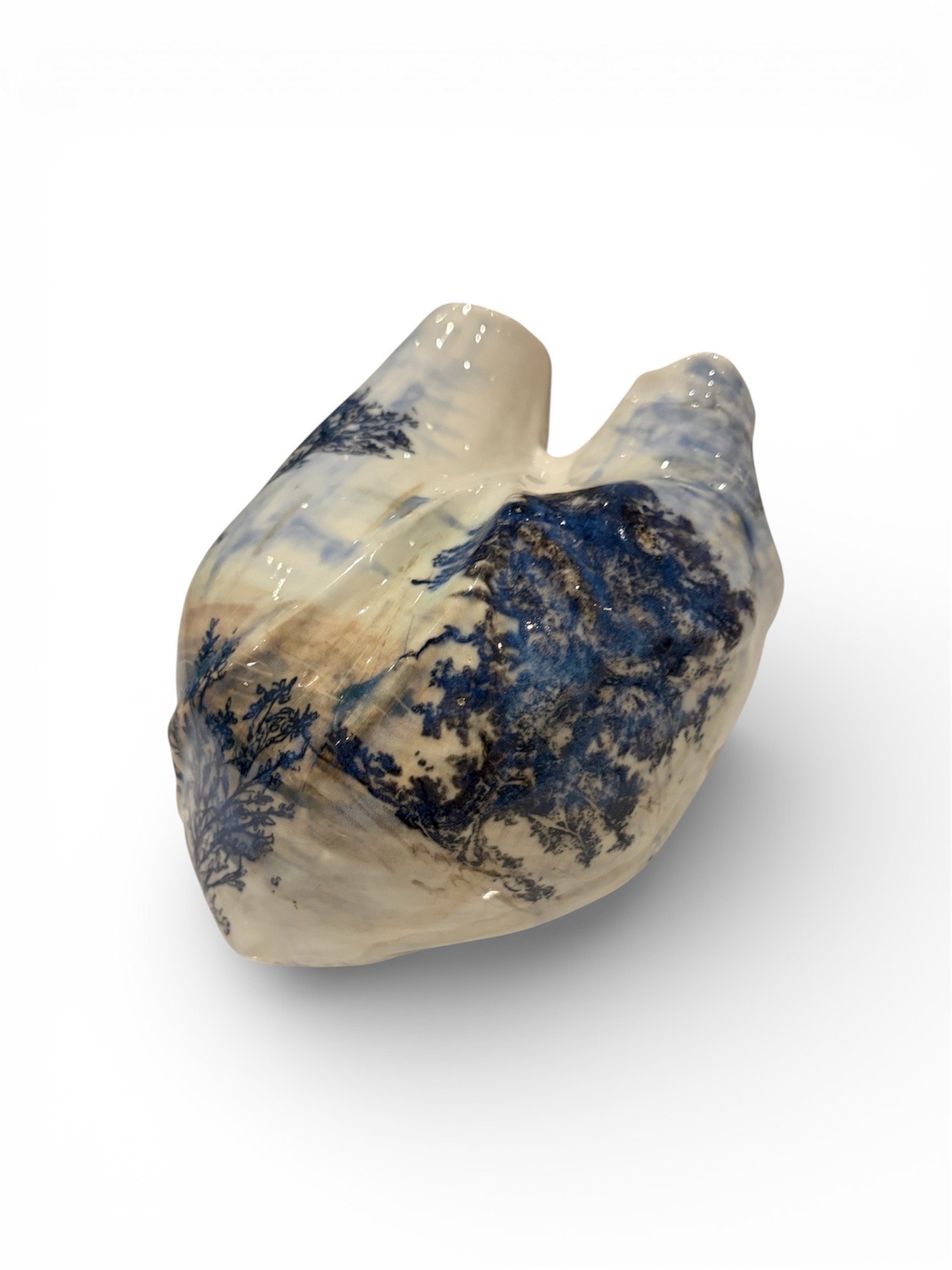 A glass sculpture of a human heart with blue and beige landscape patterns inside, resembling mountains and trees.