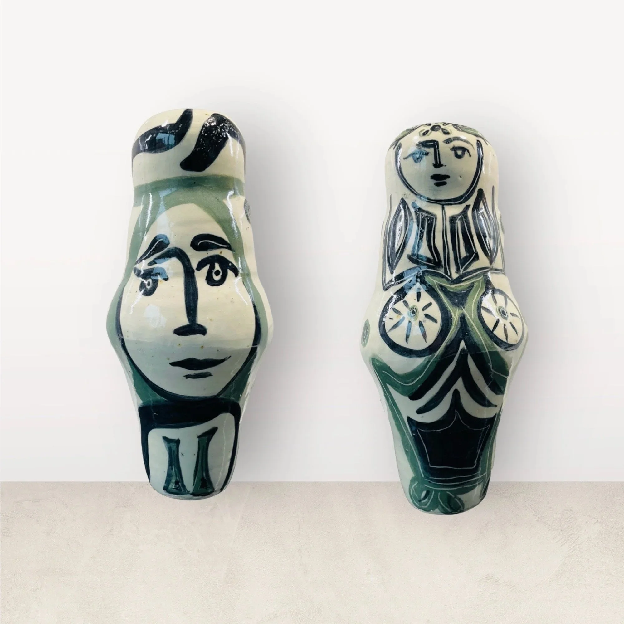 Two decorative ceramic figurines with black line artwork, one with a woman's face and the other with a stylized figure, placed against a plain white background.