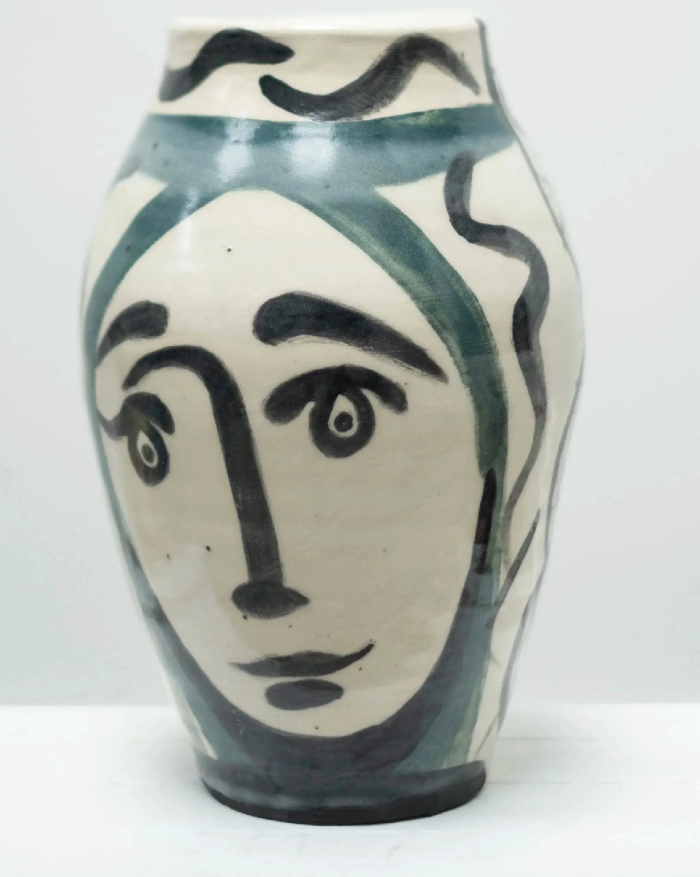 Ceramic vase with abstract face design painted in black and green on a cream background.