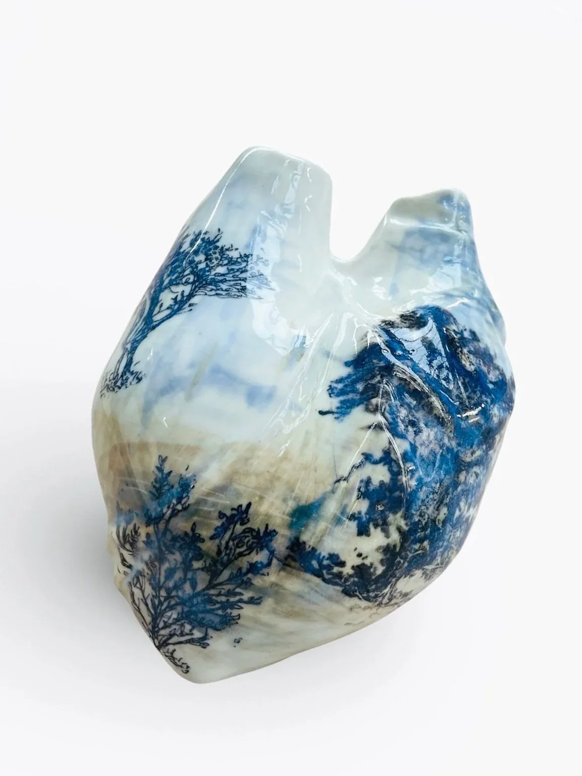 A decorative ceramic sculpture resembling a human heart, decorated with blue and white landscape scenes.