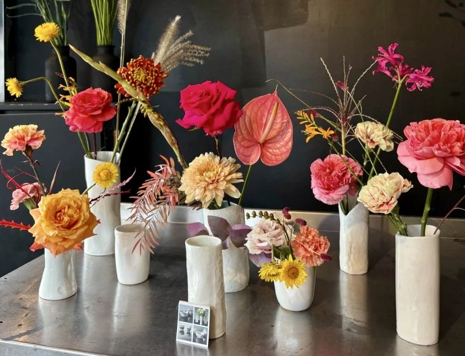 Multiple vases filled with colorful flowers including roses, carnations, and other blooms on a table with a dark background.