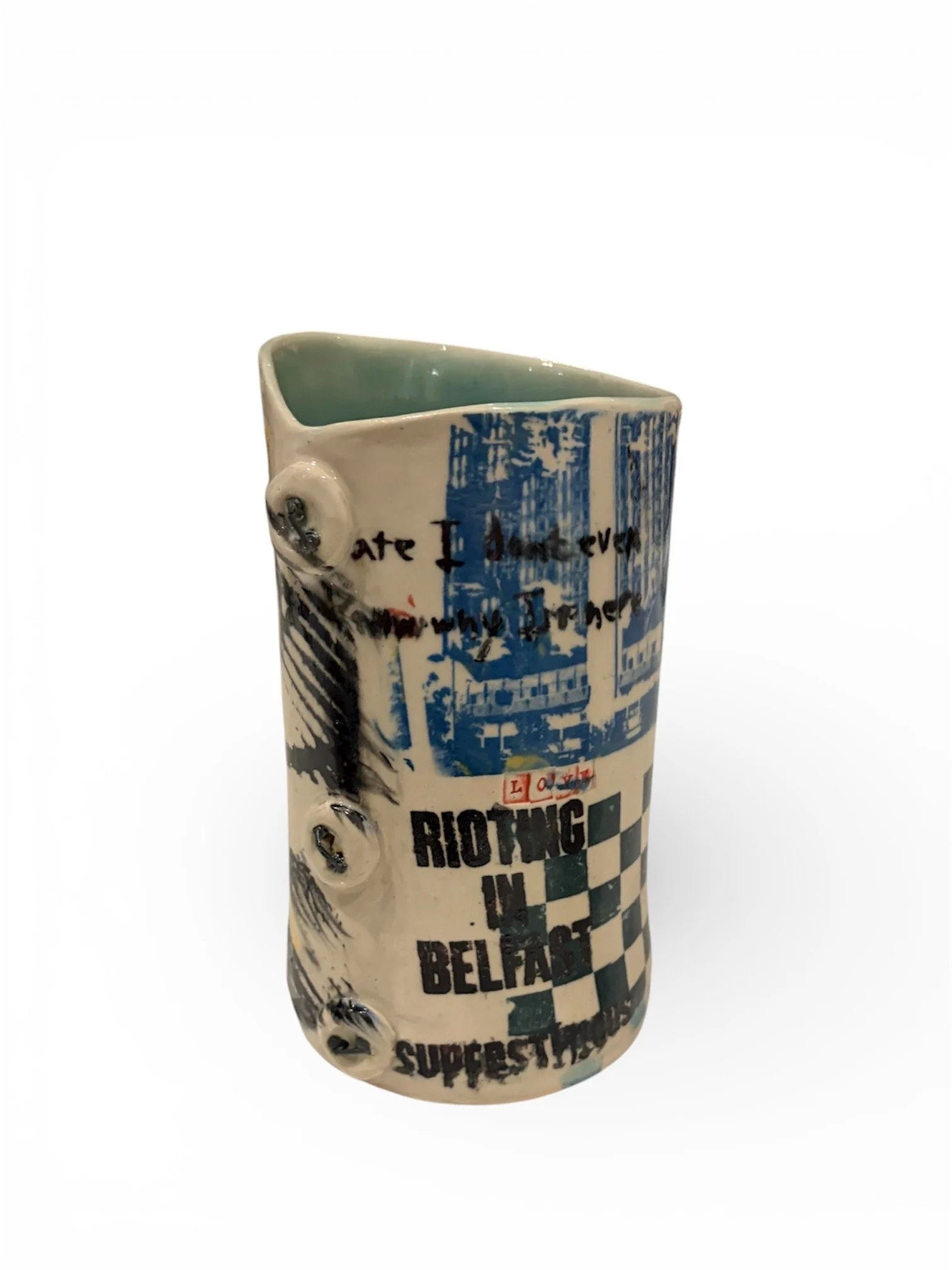 Ceramic mug with graffiti-style text and graphics, including the words 'RIOTING IN BELFAST' and 'SUPERSTORM', with various blue and black designs and a handwritten message.