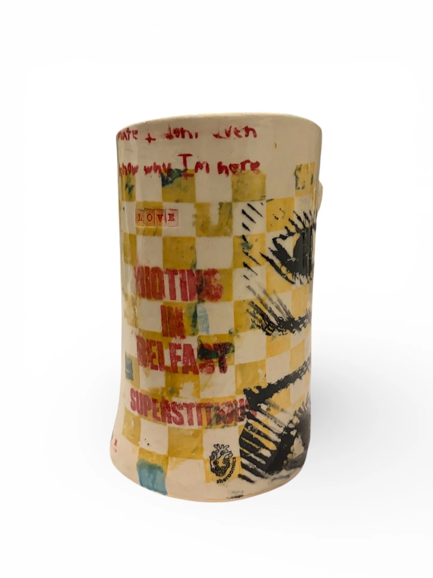 Decorative ceramic cup with abstract and graphic designs, including checkered patterns, red text, and black eye illustrations.