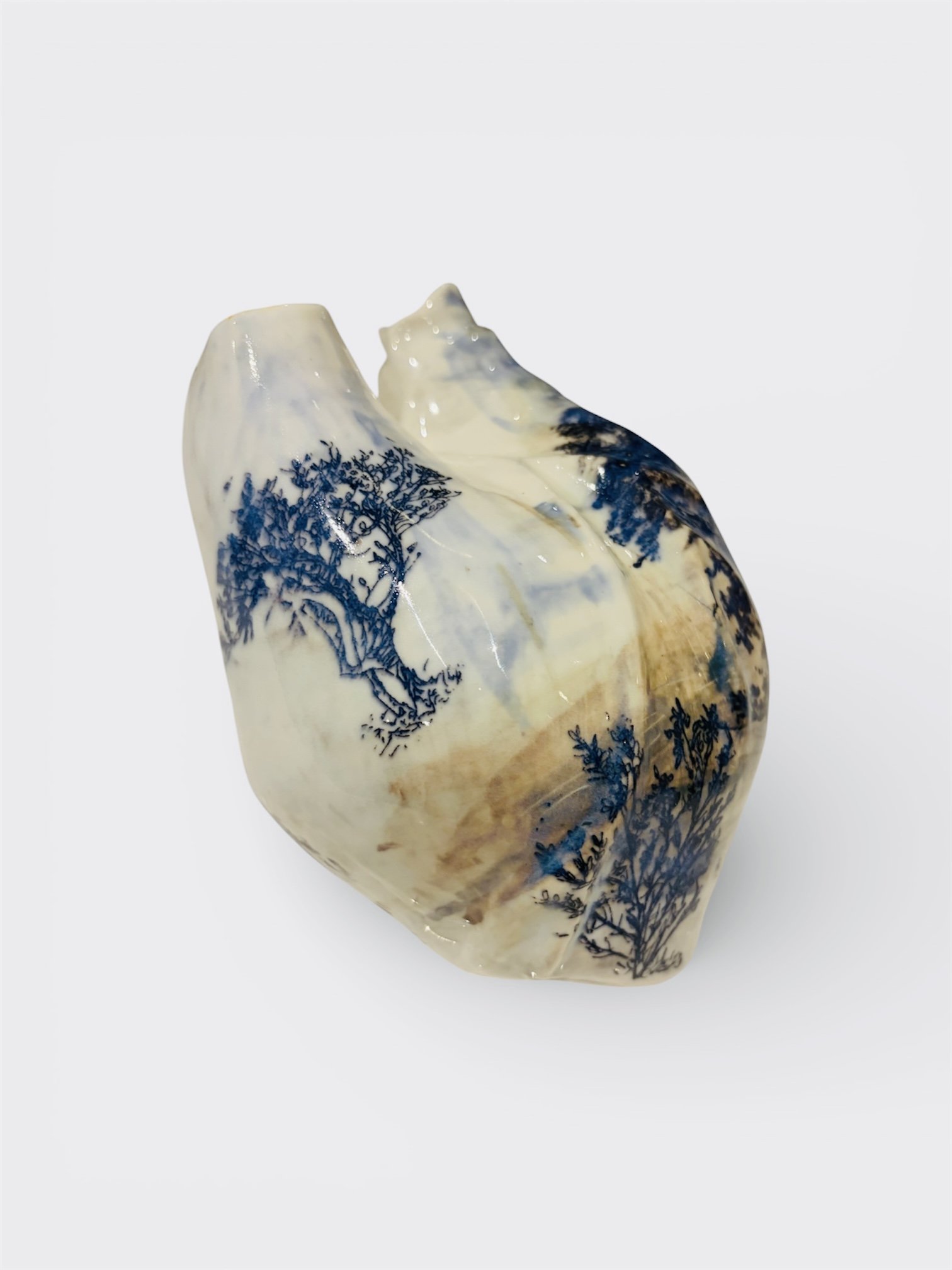 Ceramic heart sculpture with a landscape design in blue and beige tones, mounted on a white background.