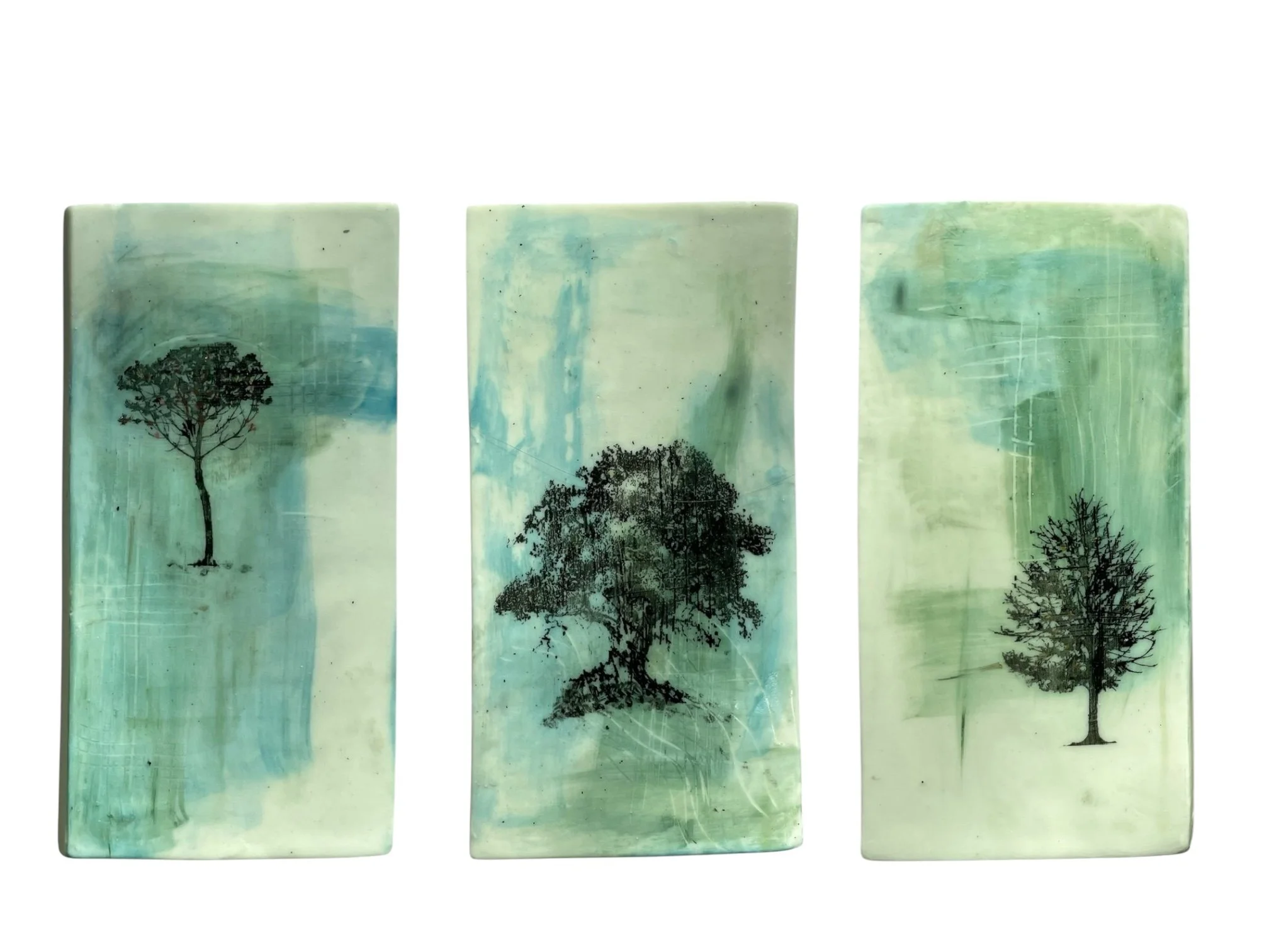 Three rectangular tiles with watercolor backgrounds in shades of green and blue, each featuring a silhouette of a tree in black.