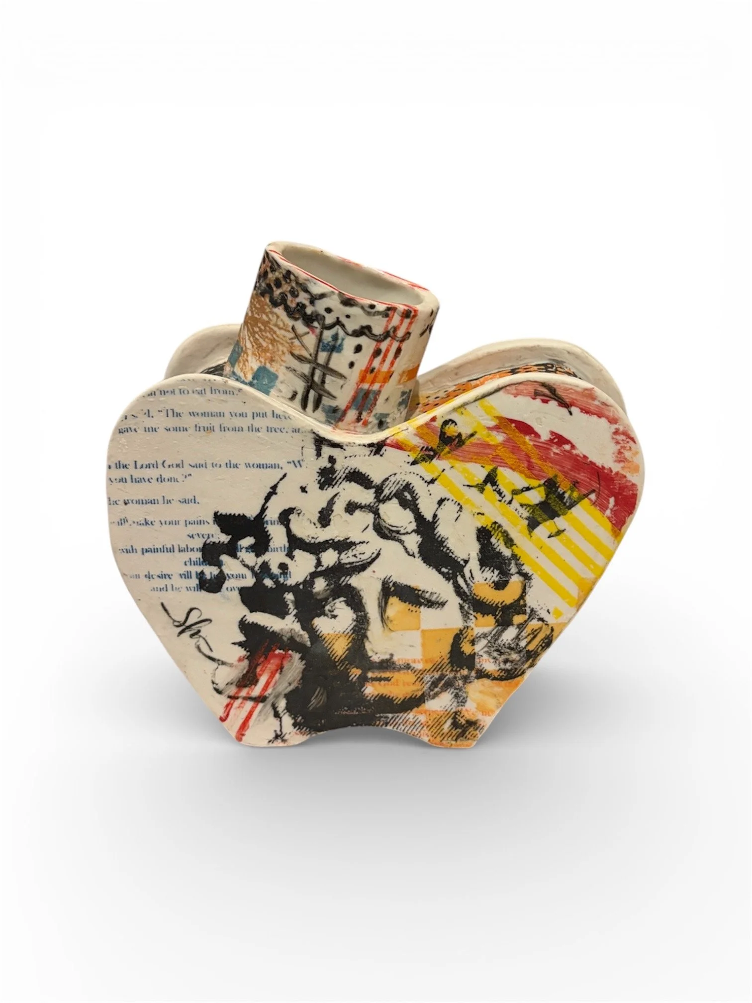 Decorative ceramic heart shaped sculpture with abstract and collage-style artwork, featuring black, red, yellow, and blue elements, including text and illustrations.