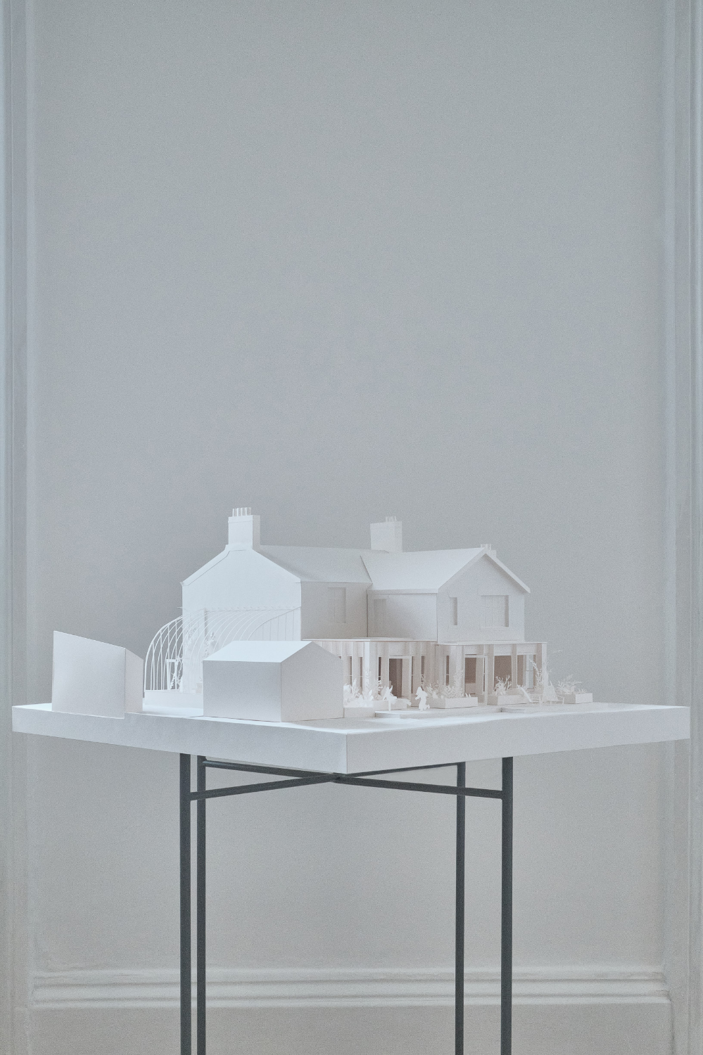 White paper model of a traditional house with a modern extension and curved glasshouse displayed on metal stand