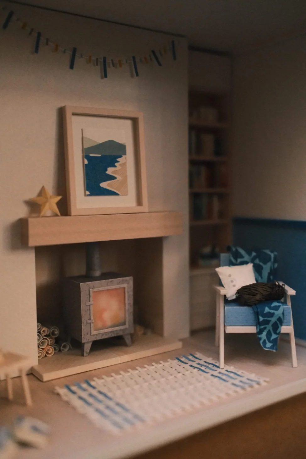 Coloured paper model of a cosy interior with log burner, chair and woven rug