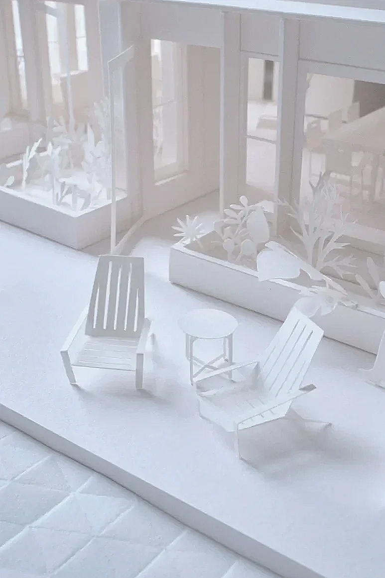 Miniature paper deck chairs and side table with raised flower beds beyond