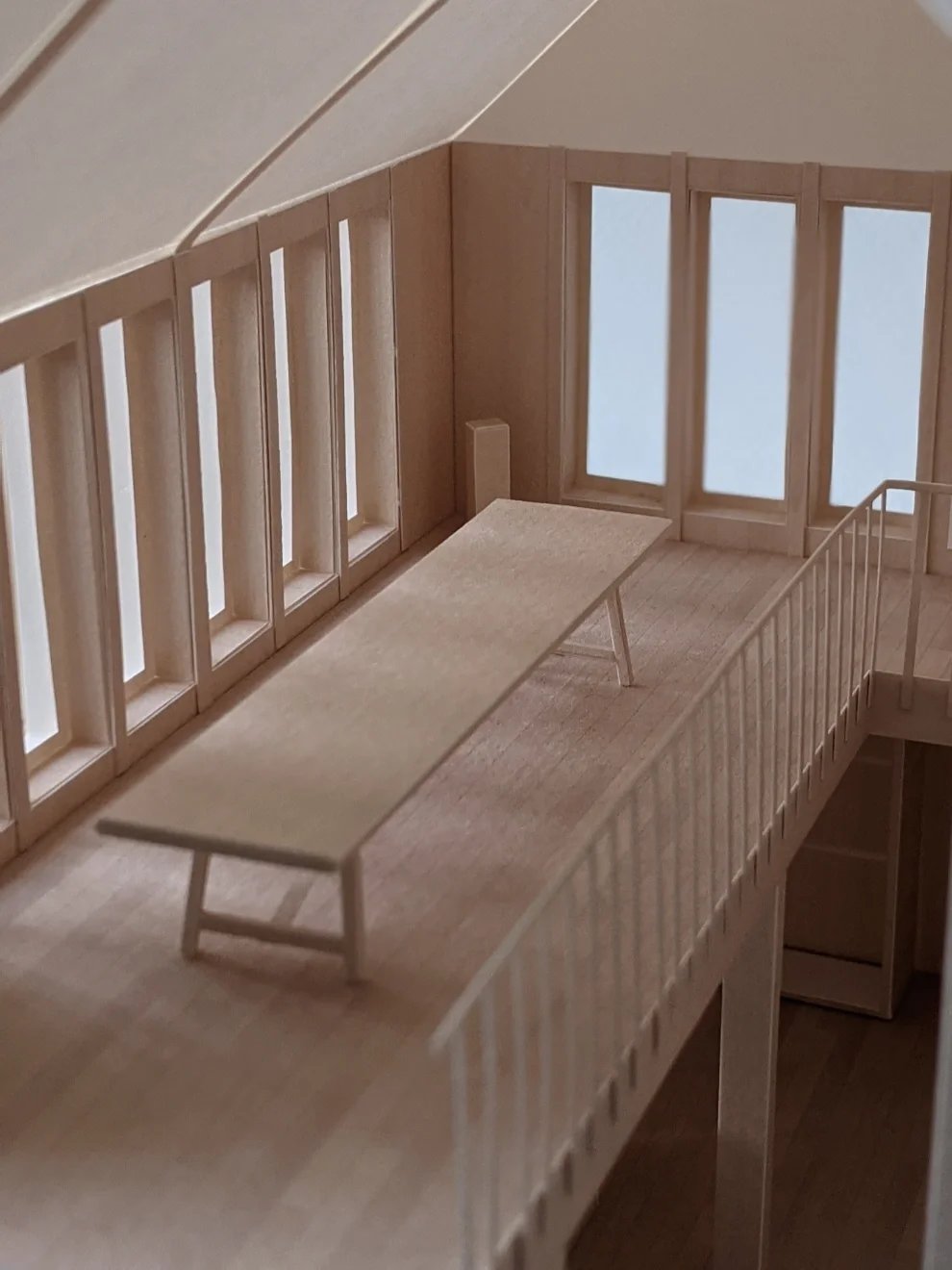 Model of a long timber exhibition table, balustrade and series of vertical windows beyond
