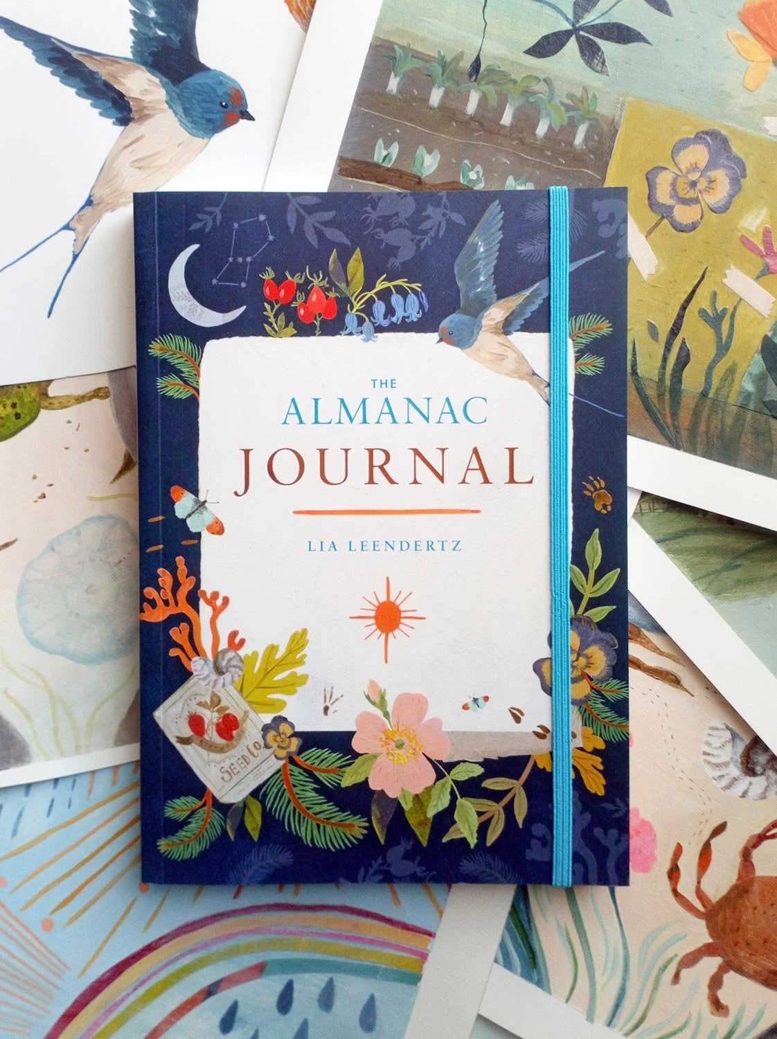 The Almanac Journal book cover sitting on top of artist portfolio sheets