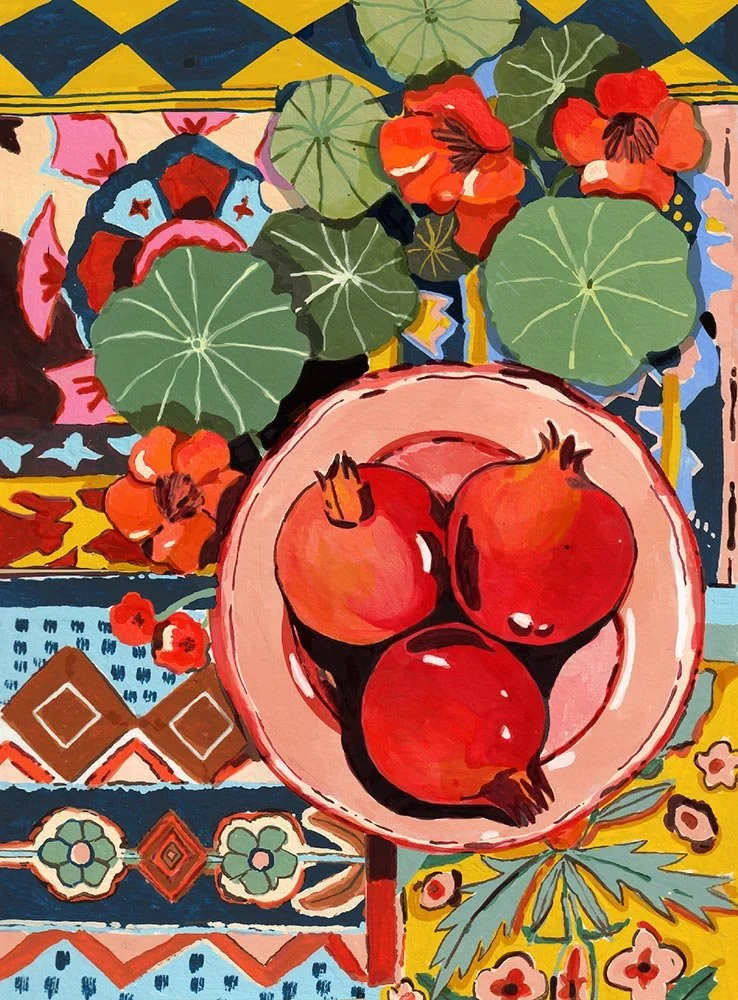 bowl of pomegranates and nasturtium plant sitting on a patterned tablecloth