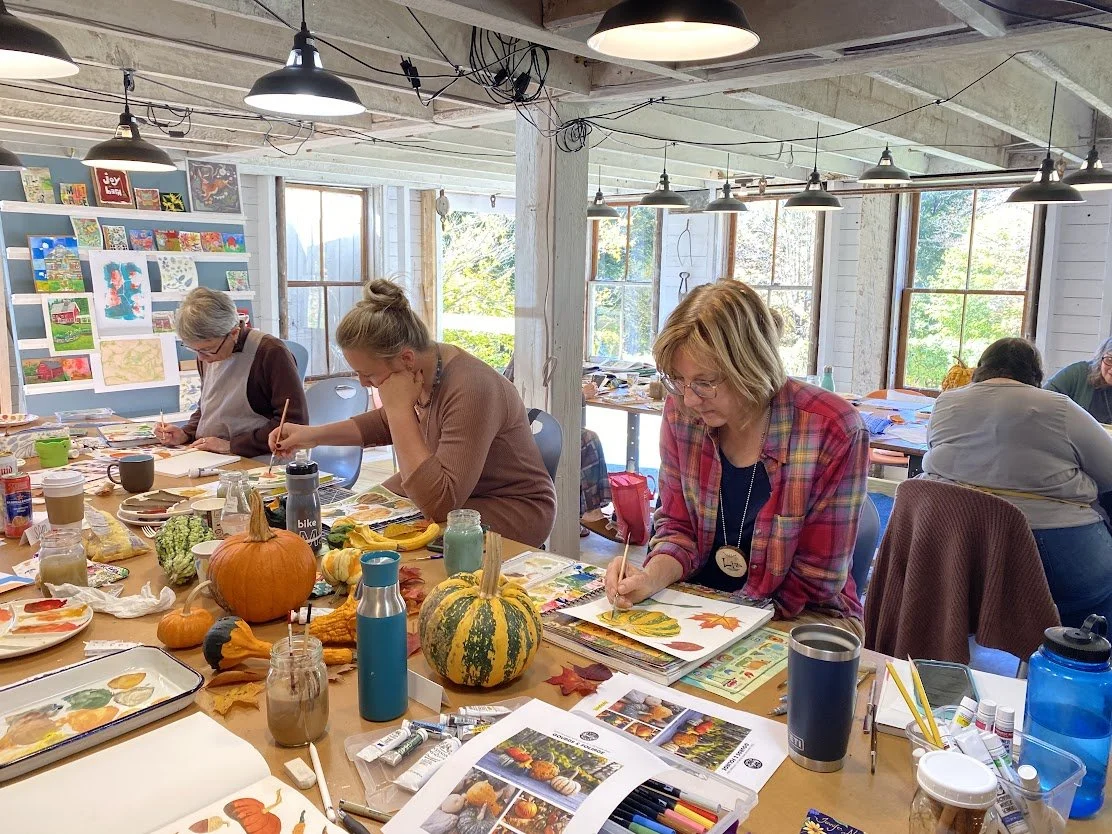 3 women painting fall gourds in cluttered art space