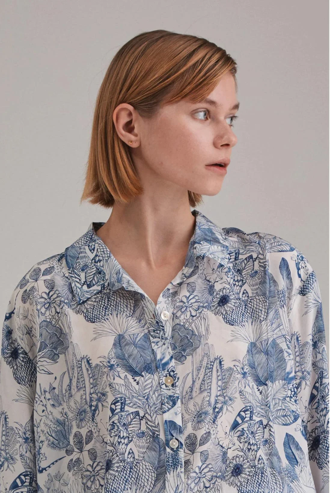 A woman with short red hair, wearing a blue and white floral button-up shirt, looking to the right.