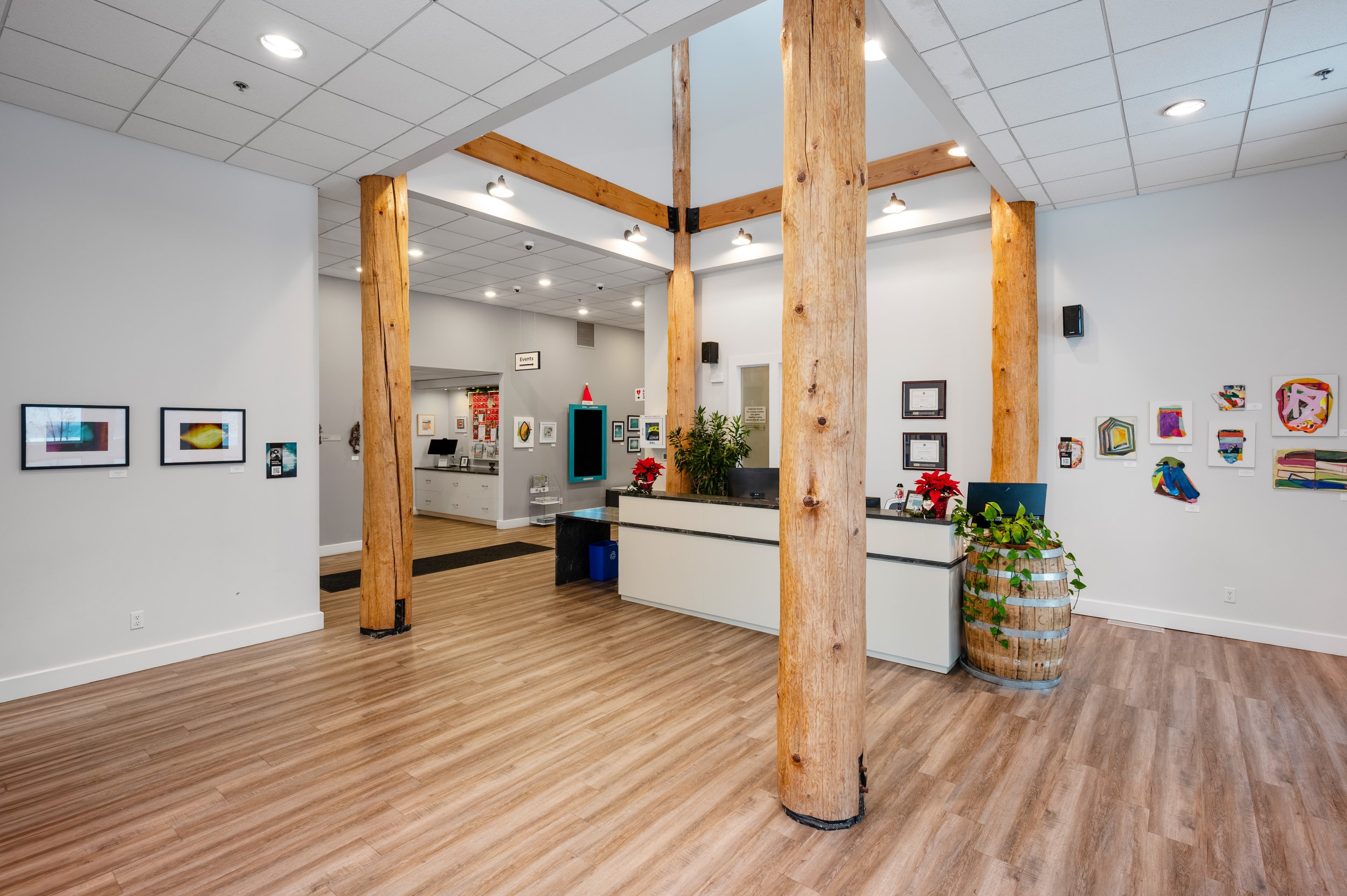 Art gallery or reception area with wooden beams, white walls, hardwood flooring, framed artwork, and a reception desk decorated with poinsettia plants.