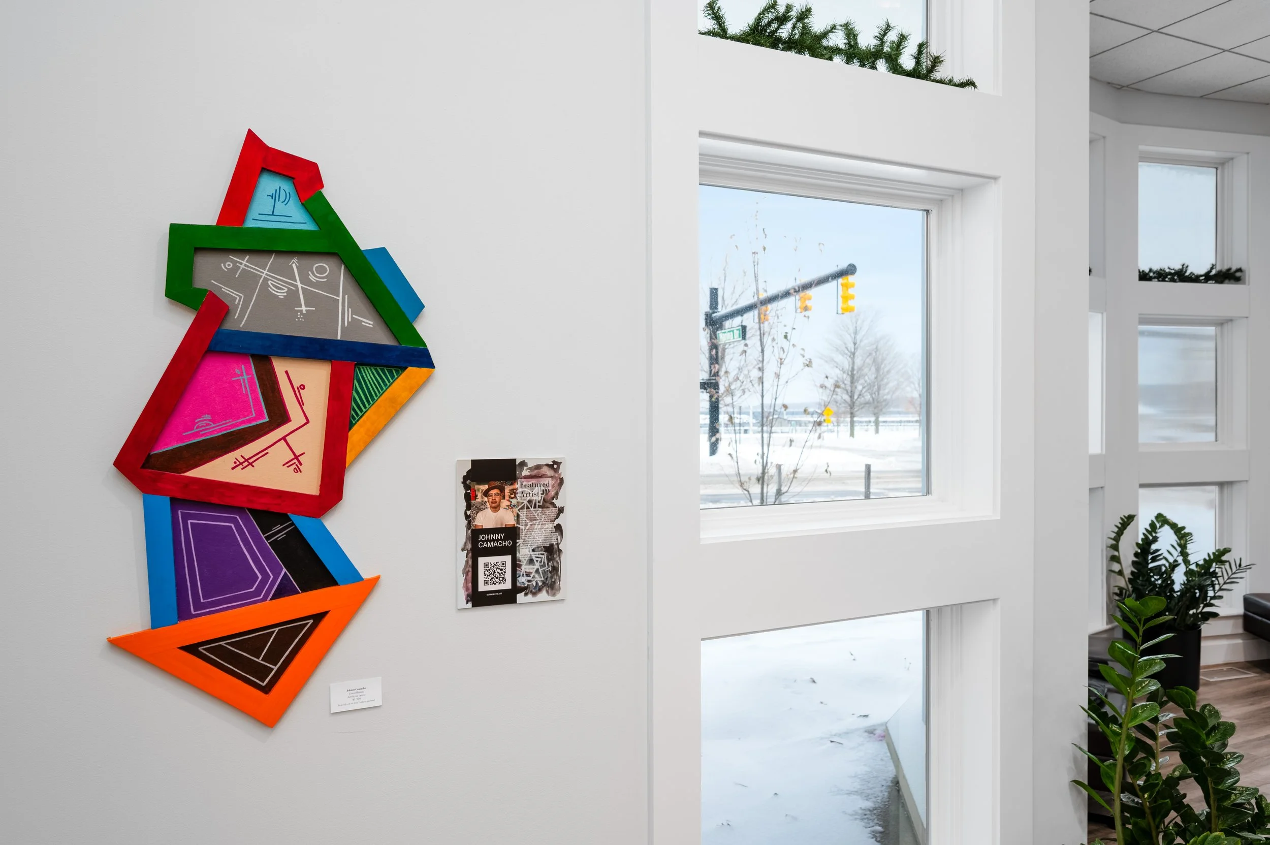 Colorful geometric wall art in an art gallery, with windows showing a snowy outdoor scene with trees and a traffic light.
