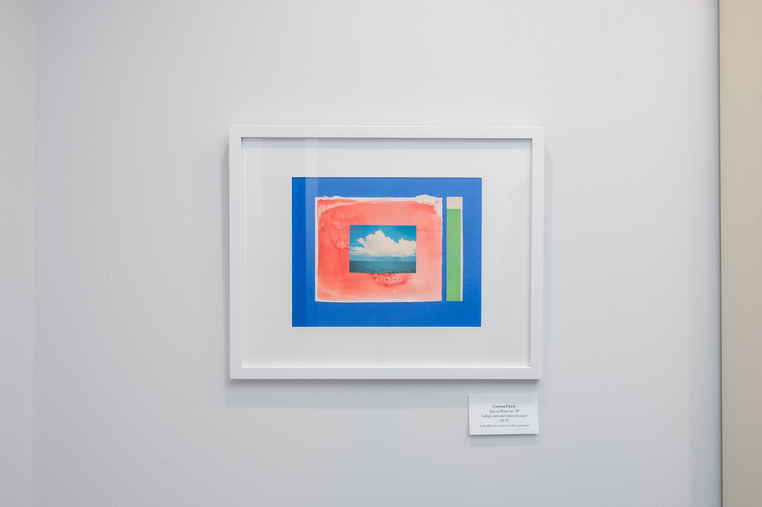 Colorful artwork in a white frame on a white wall, featuring a central image of the sky with clouds, surrounded by abstract shapes in red, blue, and green.