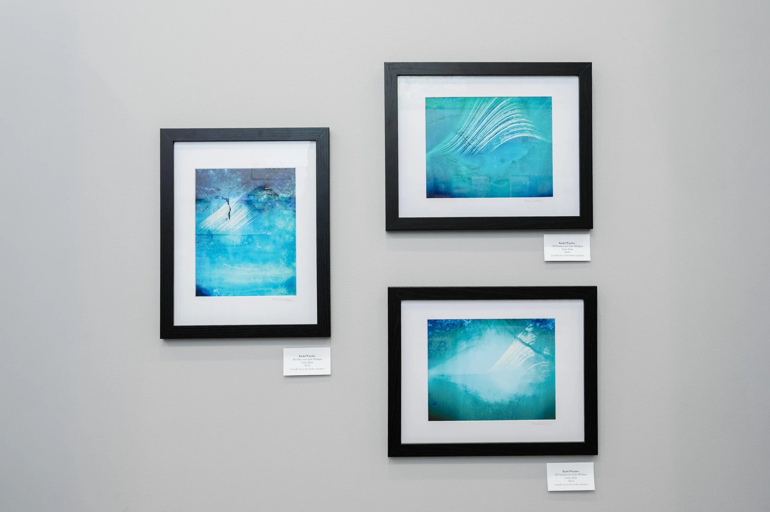 Three framed blue abstract paintings on a light gray gallery wall.