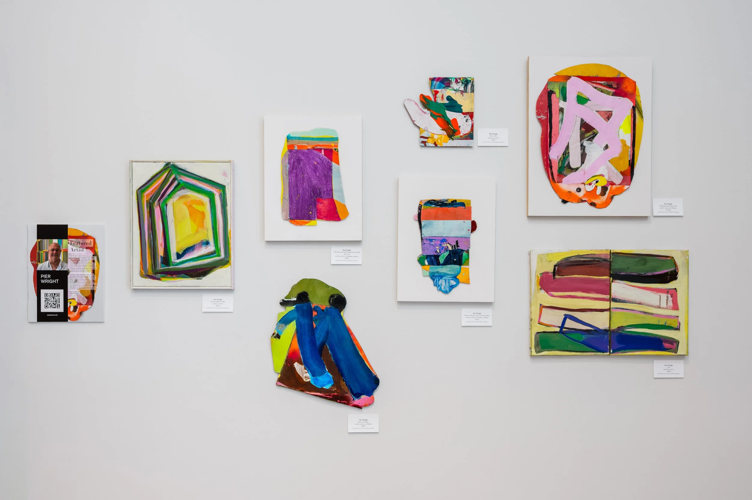 Collection of abstract colorful paintings and cutouts on a white gallery wall.