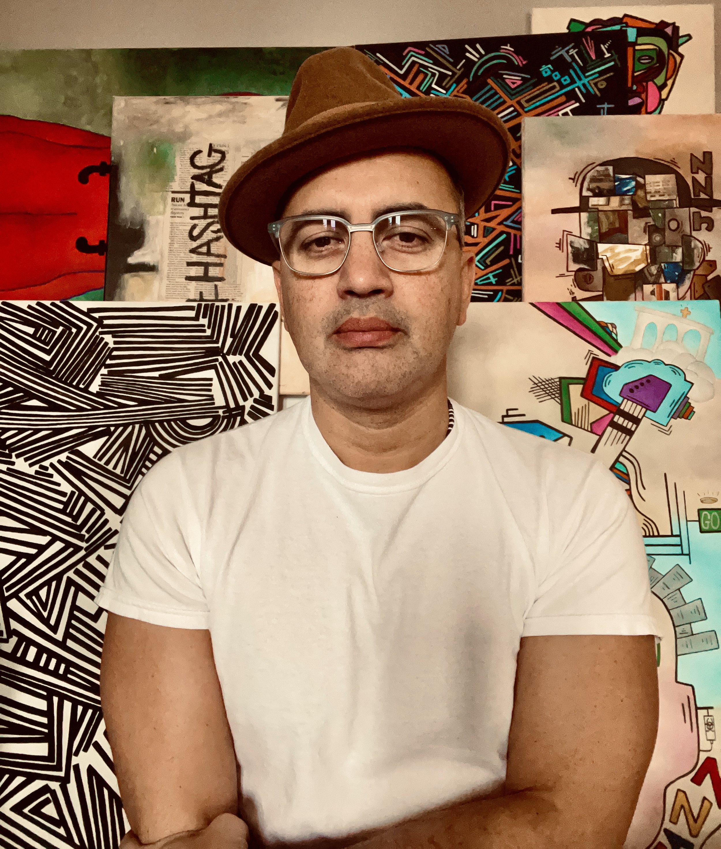 A person wearing a brown hat and glasses, standing in front of colorful abstract and graffiti-style artwork.