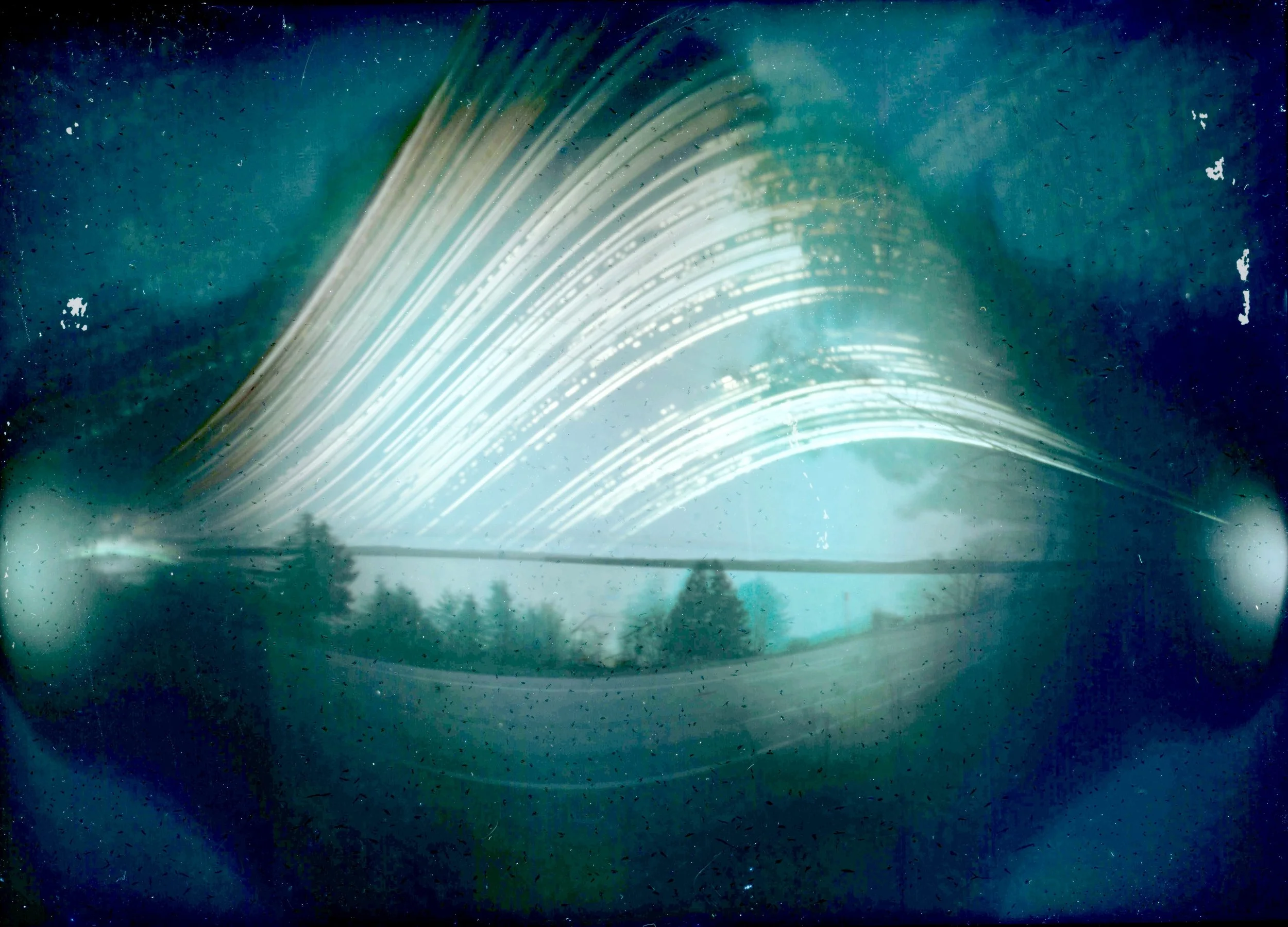 Light trails and streaks in the night sky with silhouettes of trees and power lines at the bottom.