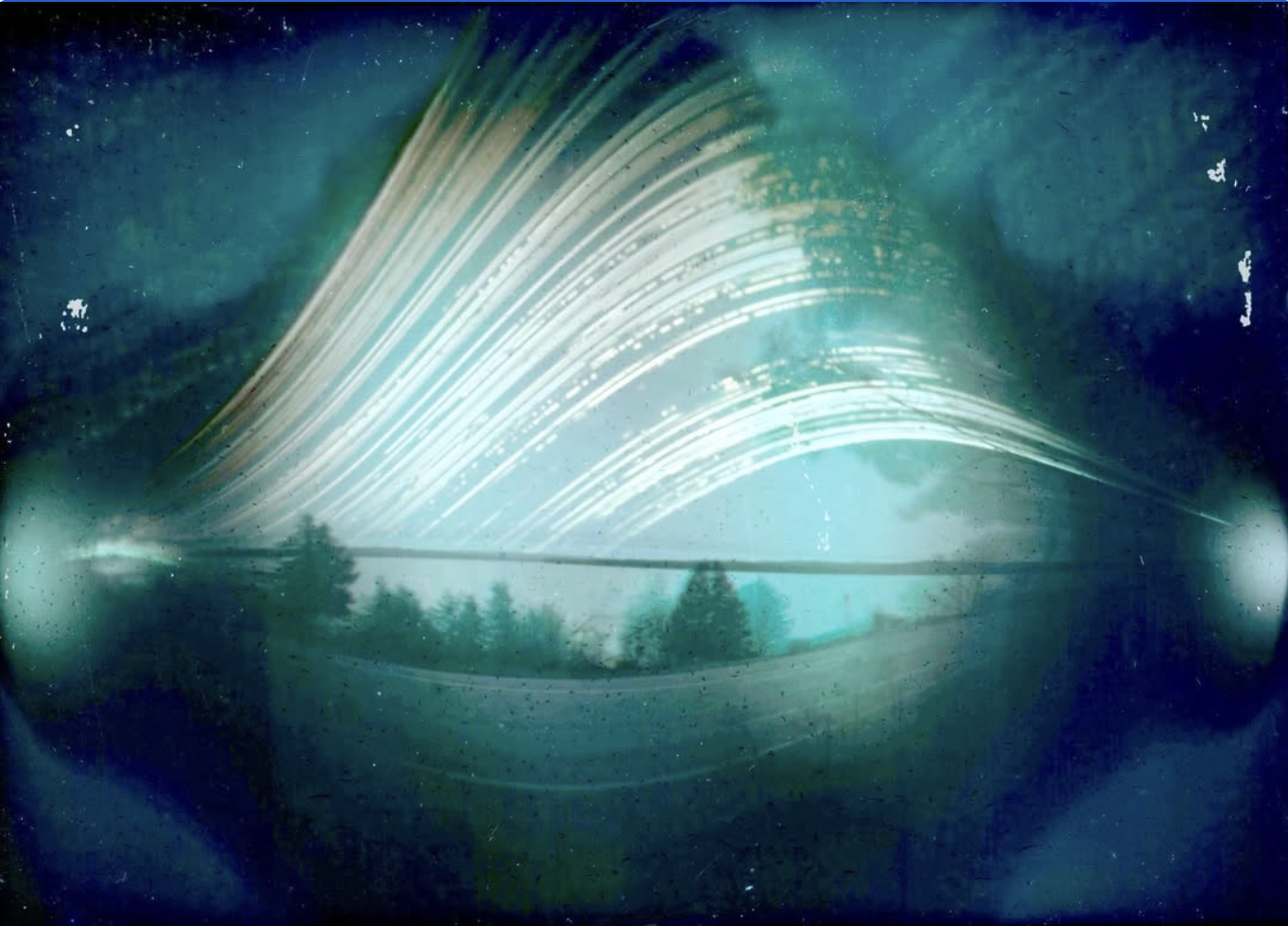 Long exposure photo of star trails over a bridge and a calm lake with trees, viewed through a pair of sunglasses.