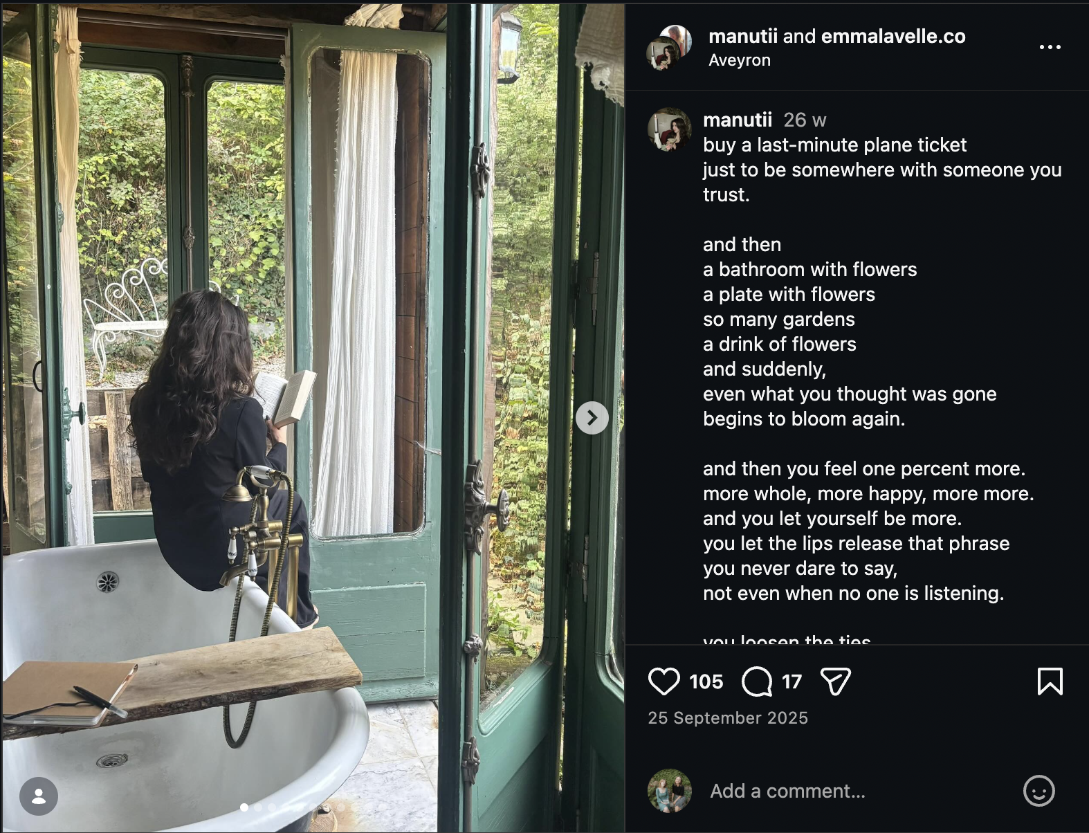 A person with long dark hair reading a book while sitting on the edge of a vintage bathtub with a rustic wooden shelf, inside a green-framed glass-enclosed room with a garden view.