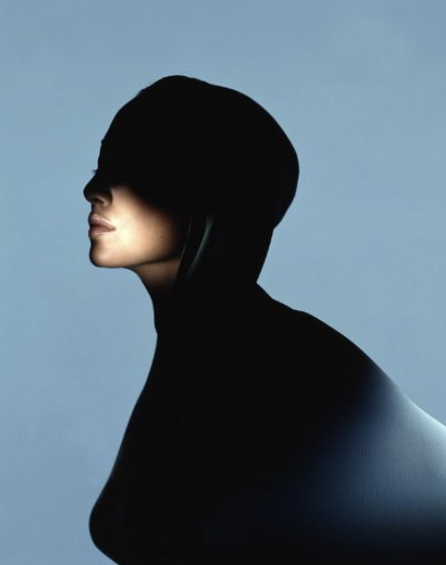 Side profile of a woman wearing a black hat and a black outfit against a plain light blue background.