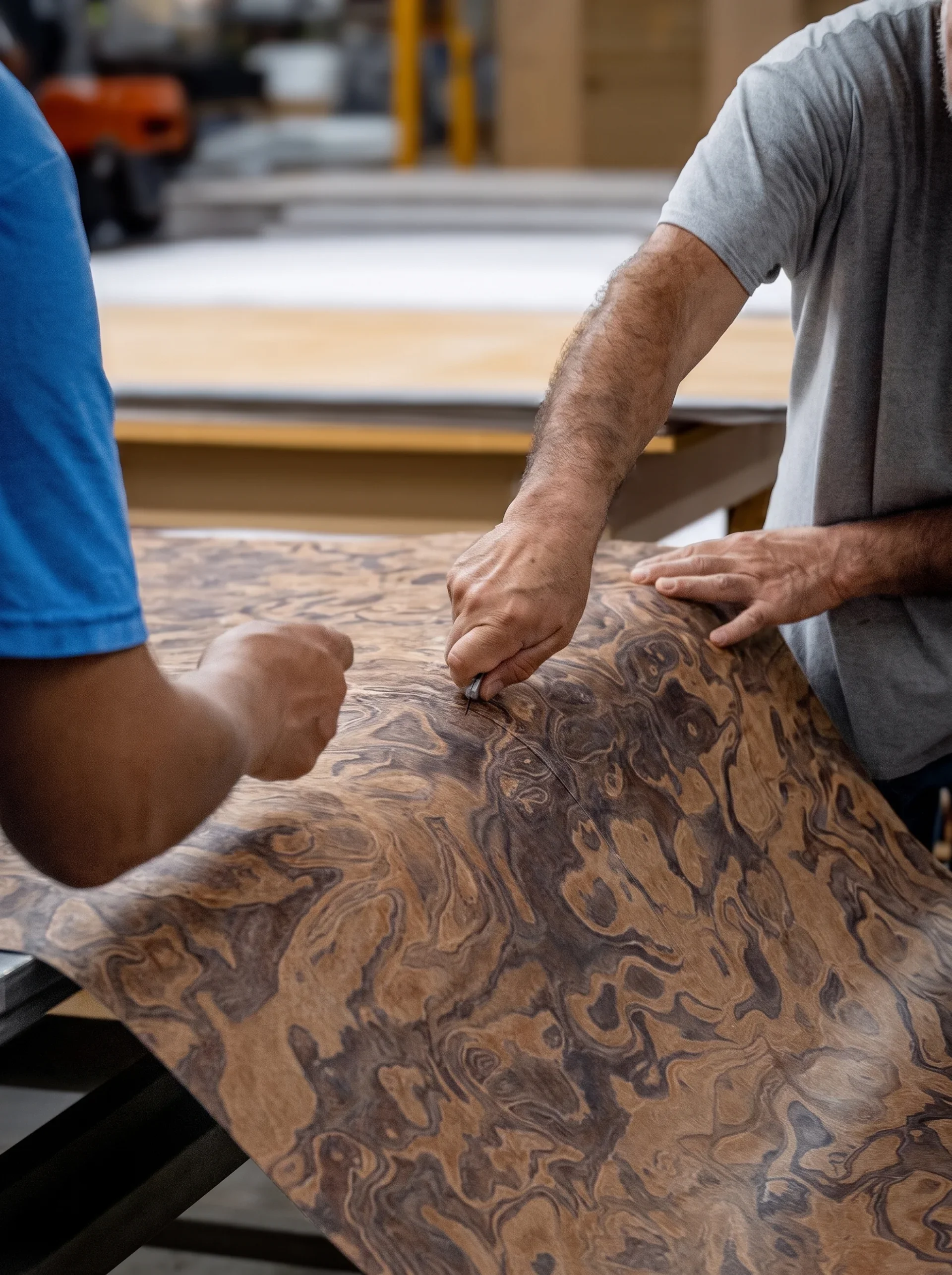 People working on a wood project in a workshop, focusing on a wooden surface with a swirling grain pattern.