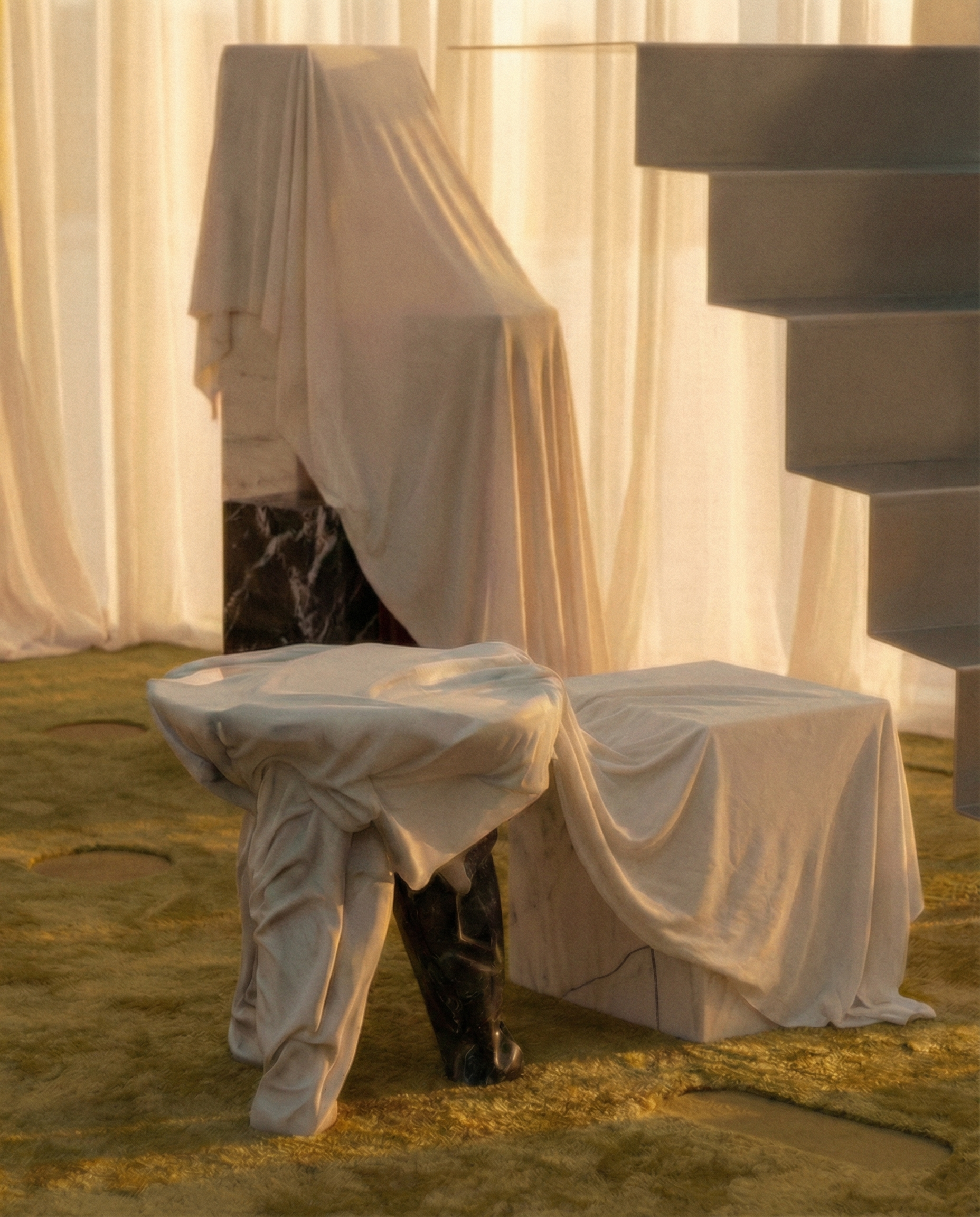 Club chair draped with a white slipcover in a room with sheer curtains, stacks of white boxes, and a person wearing black boots and beige pants.