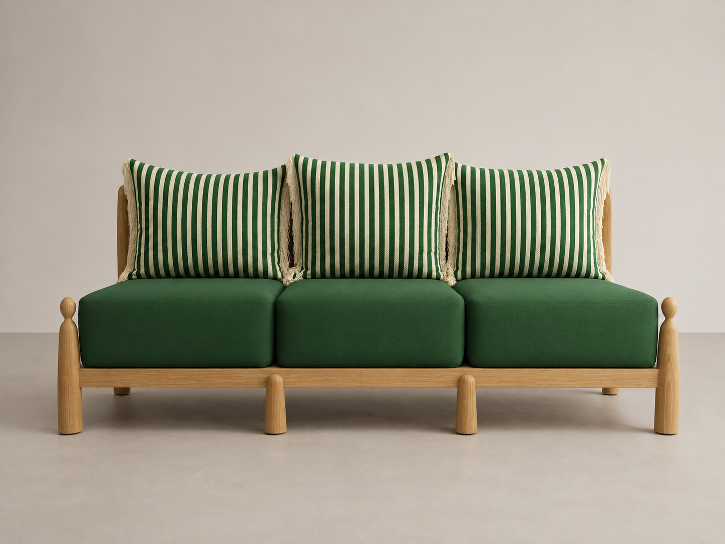 A green sofa with three green and white striped pillows with tassels, on a light-colored floor against a plain wall.