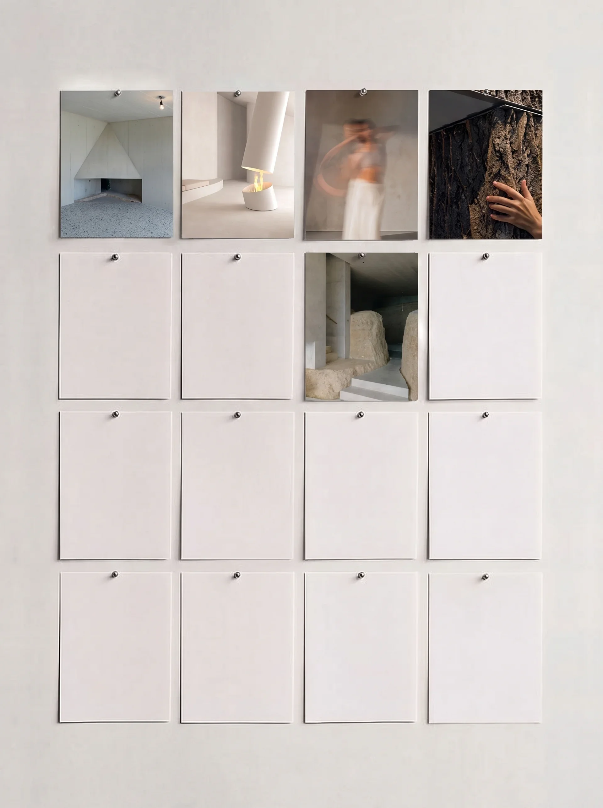 A wall display with six small square compartments; four of them have photographs behind glass, one has rocks and concrete, and one is empty. The photographs depict a minimalist interior with white walls and fixtures, a person taking a selfie with a b
