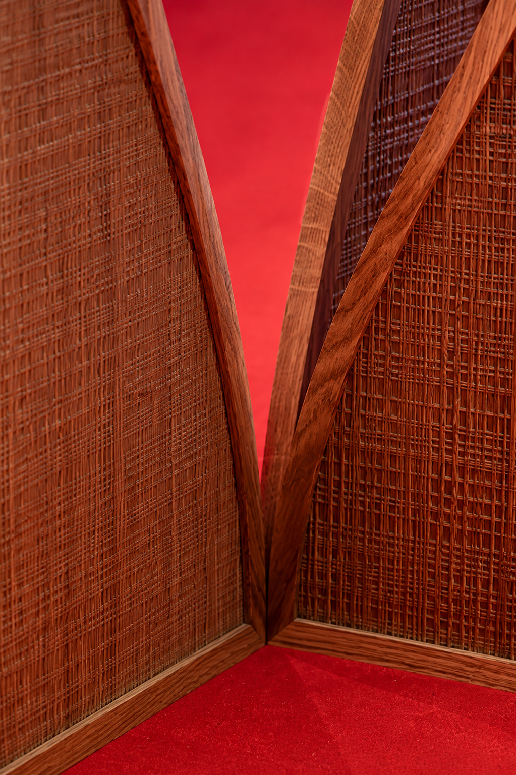 Close-up of wooden room divider with woven rattan panels and a diagonal wooden frame, on a red carpet.