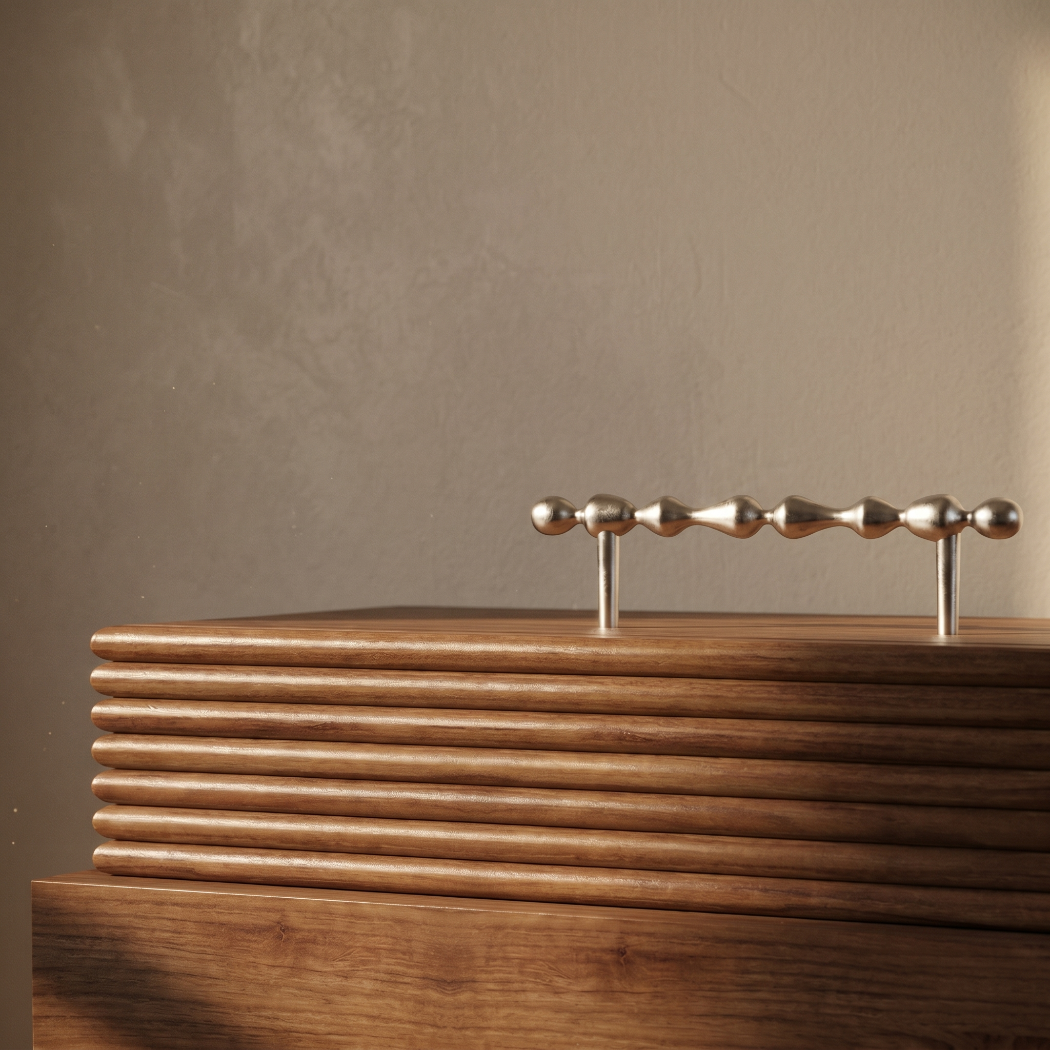 A metal sculpture with a row of connected, rounded, metallic beads on a horizontal shaft, mounted on a wooden base, set against a plain, beige wall.