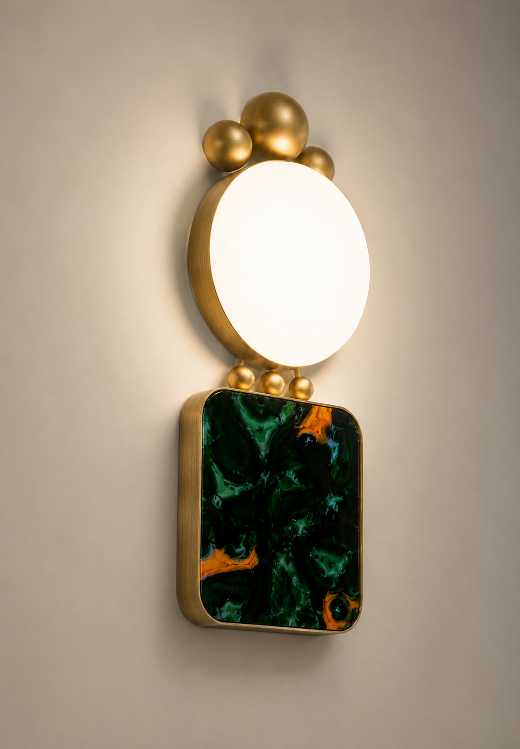 Decorative wall light fixture with a round white light surrounded by gold spheres and a rectangular green and orange marbled element below.