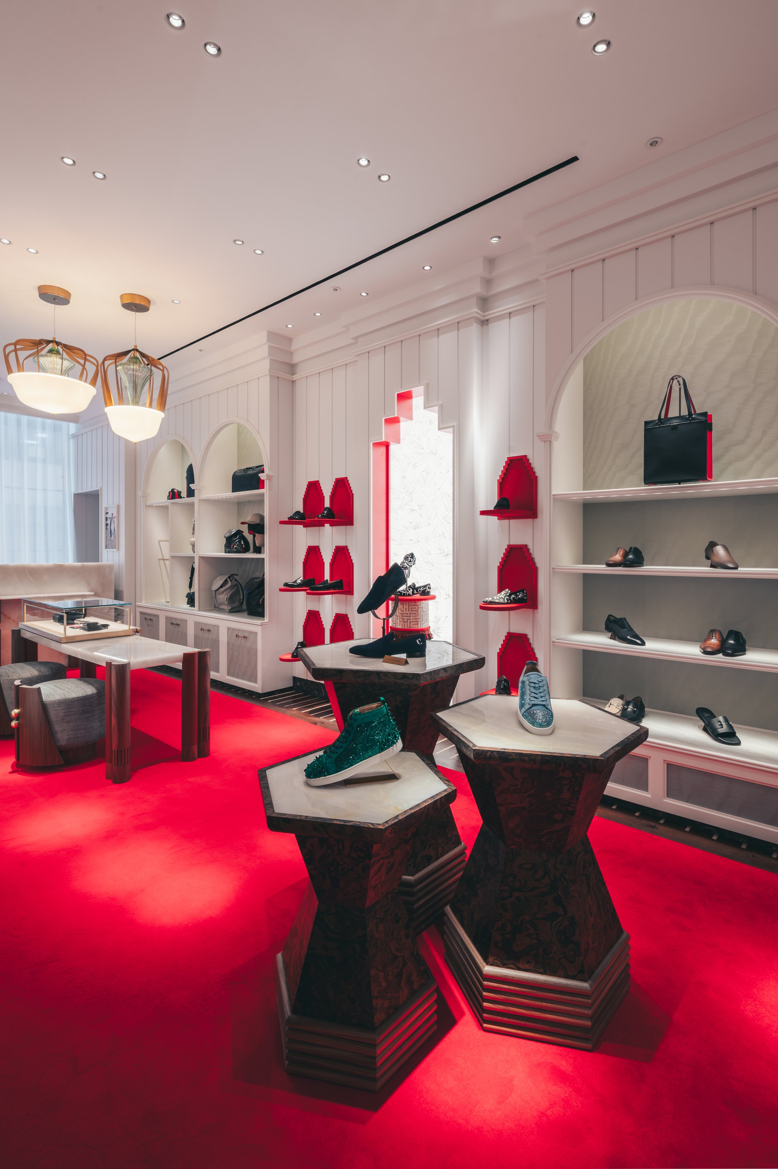 Interior view of a shoe store with white walls, red display shelves, and a red carpeted floor. Shoes are displayed on tables and shelves, and a bag is on a shelf in an arched alcove.