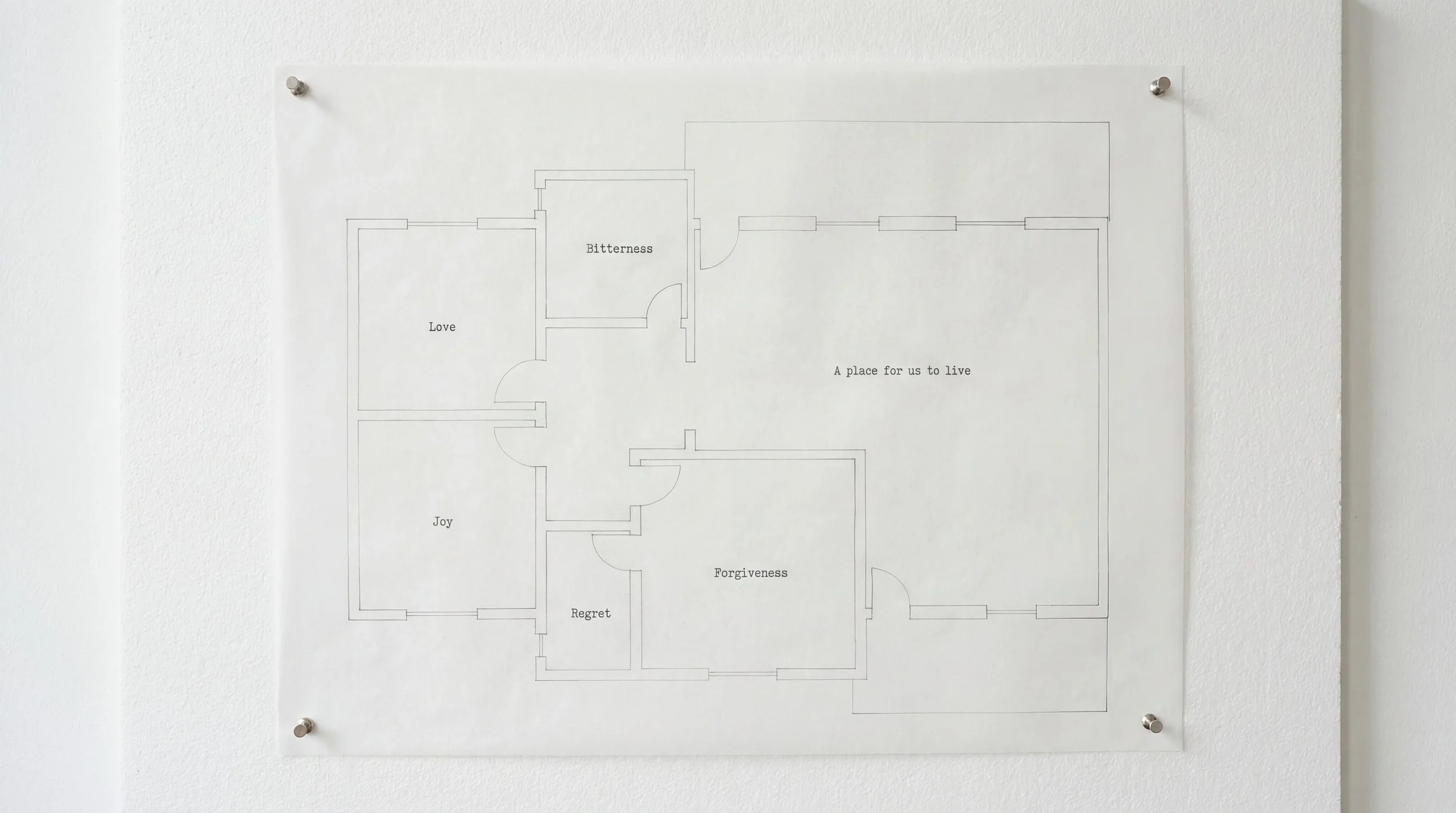A floor plan drawing of a house layout displayed on a white wall, pinned at each corner with silver pins.