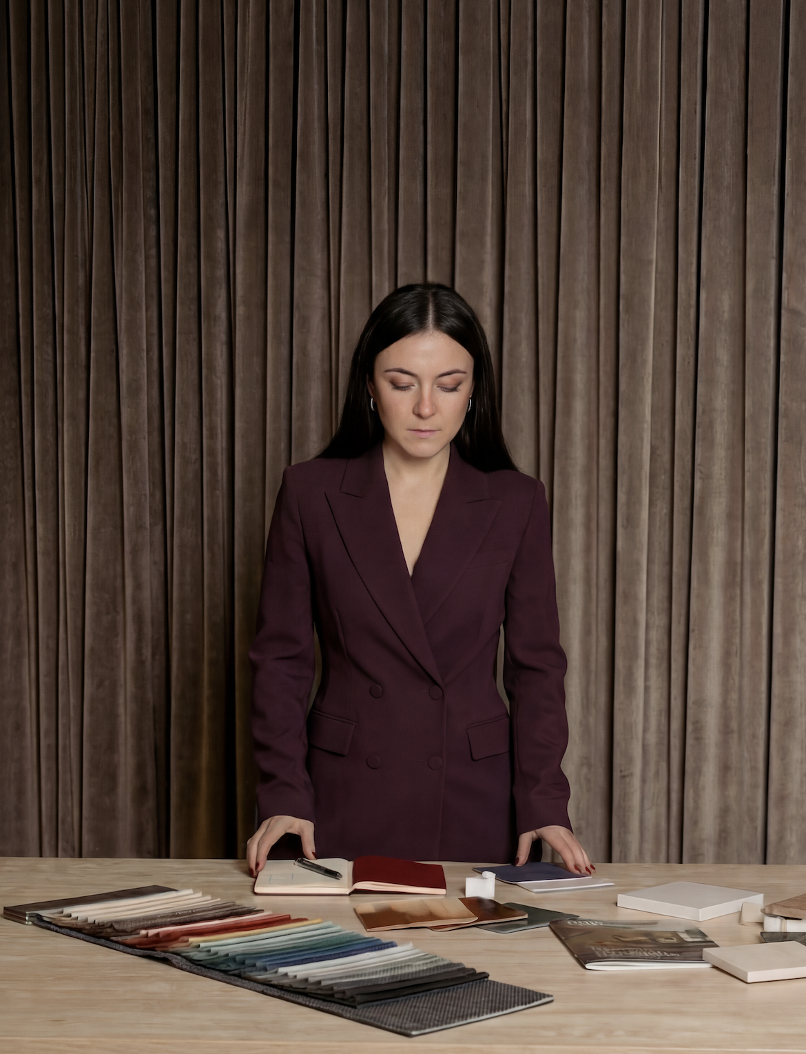 A woman in a maroon blazer looking down at fabric samples and color swatches on a table.