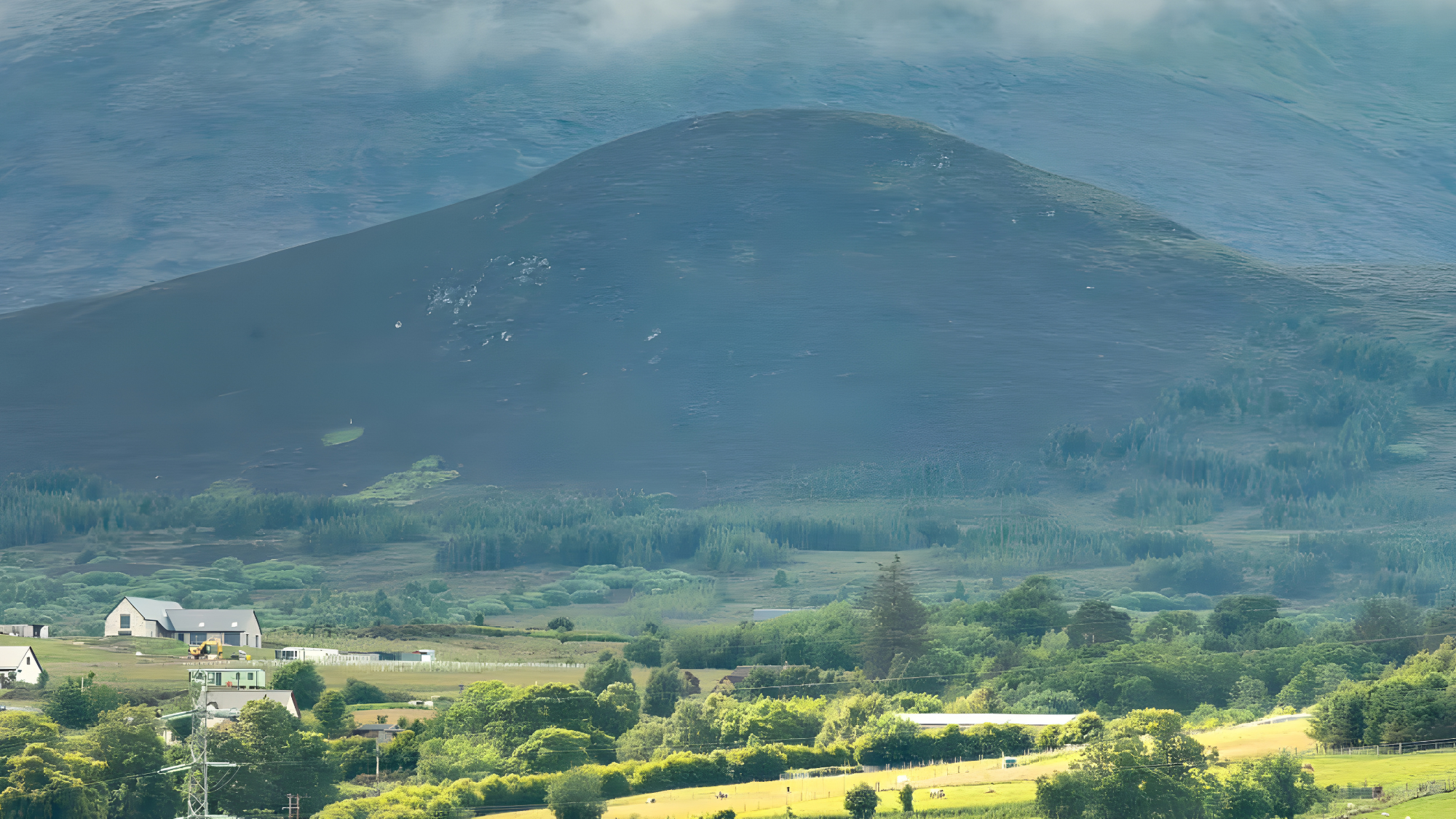Scenic landscape near Dundee showing farm buildings, trees, and fields with a large mountain in the background, photographed by Kaelyn Robertson Sakura Property Collective, estate agents in Dundee & St Andrews.